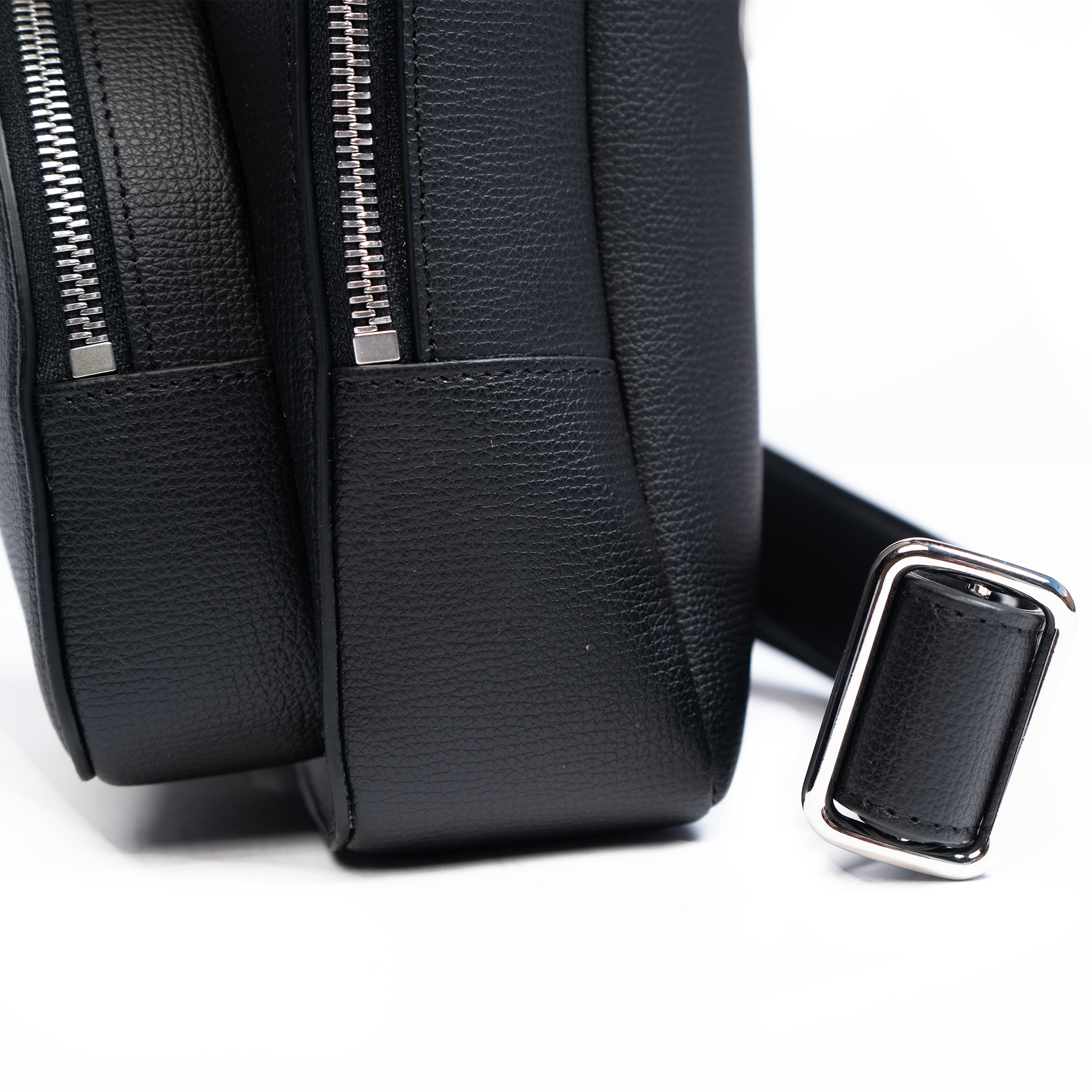 A jet black, leather backpack with a front pocket and a central zipper closure. The backpack features a compact design suitable for personal use.