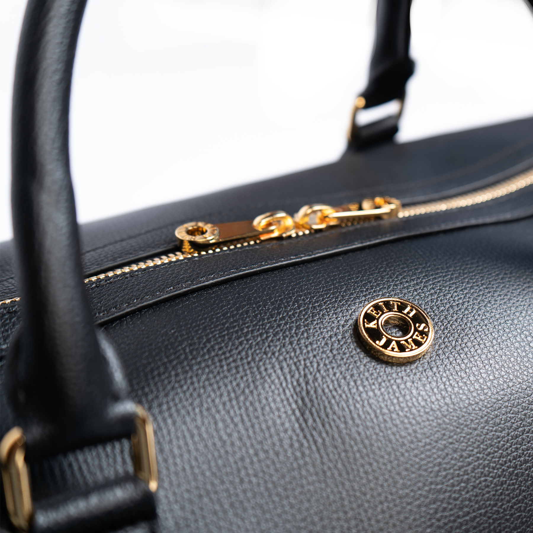 A jet black duffel bag with a detachable strap and gold-tone hardware on a white background.