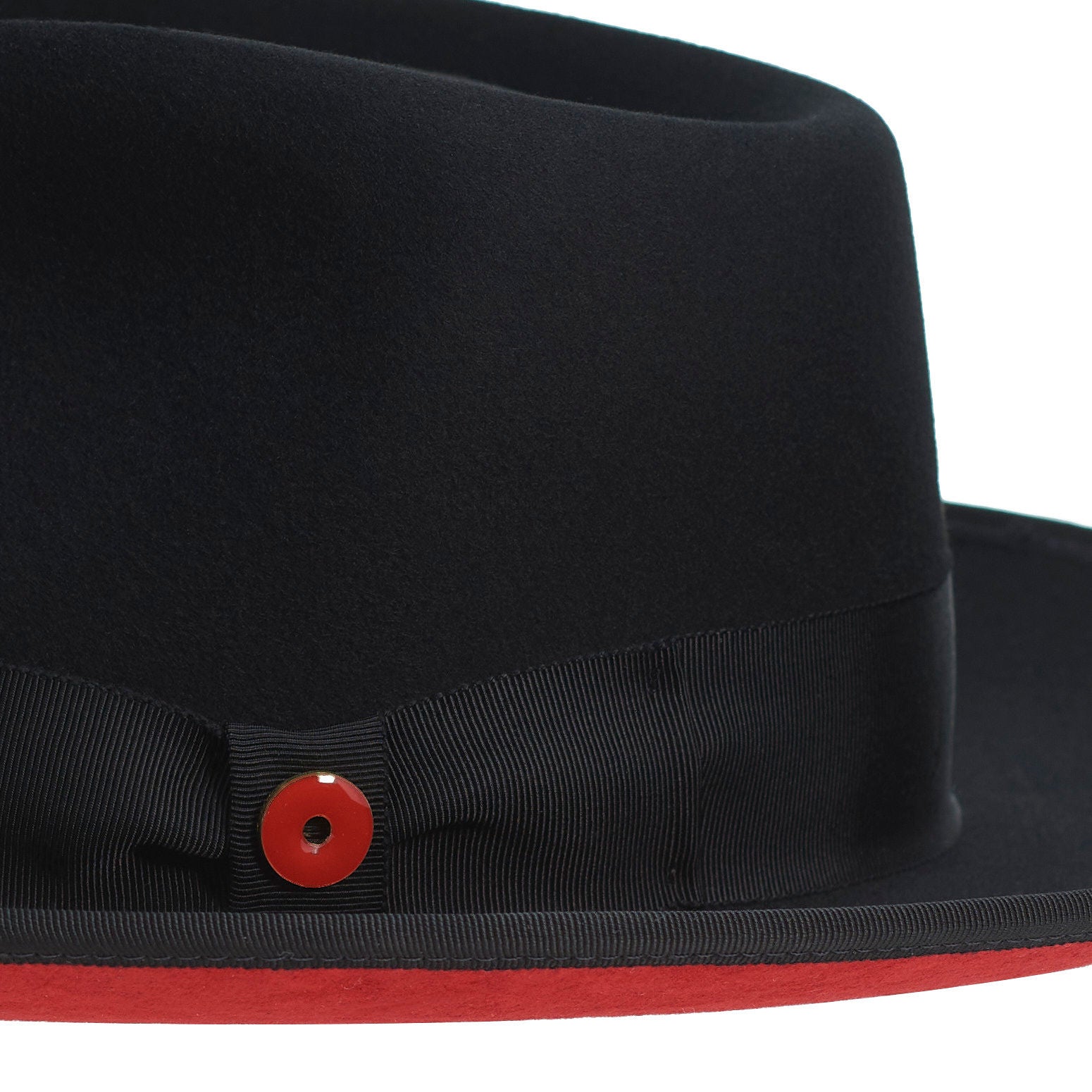 A classic black hat with a red bottom brim and a signature logo pin on the side.