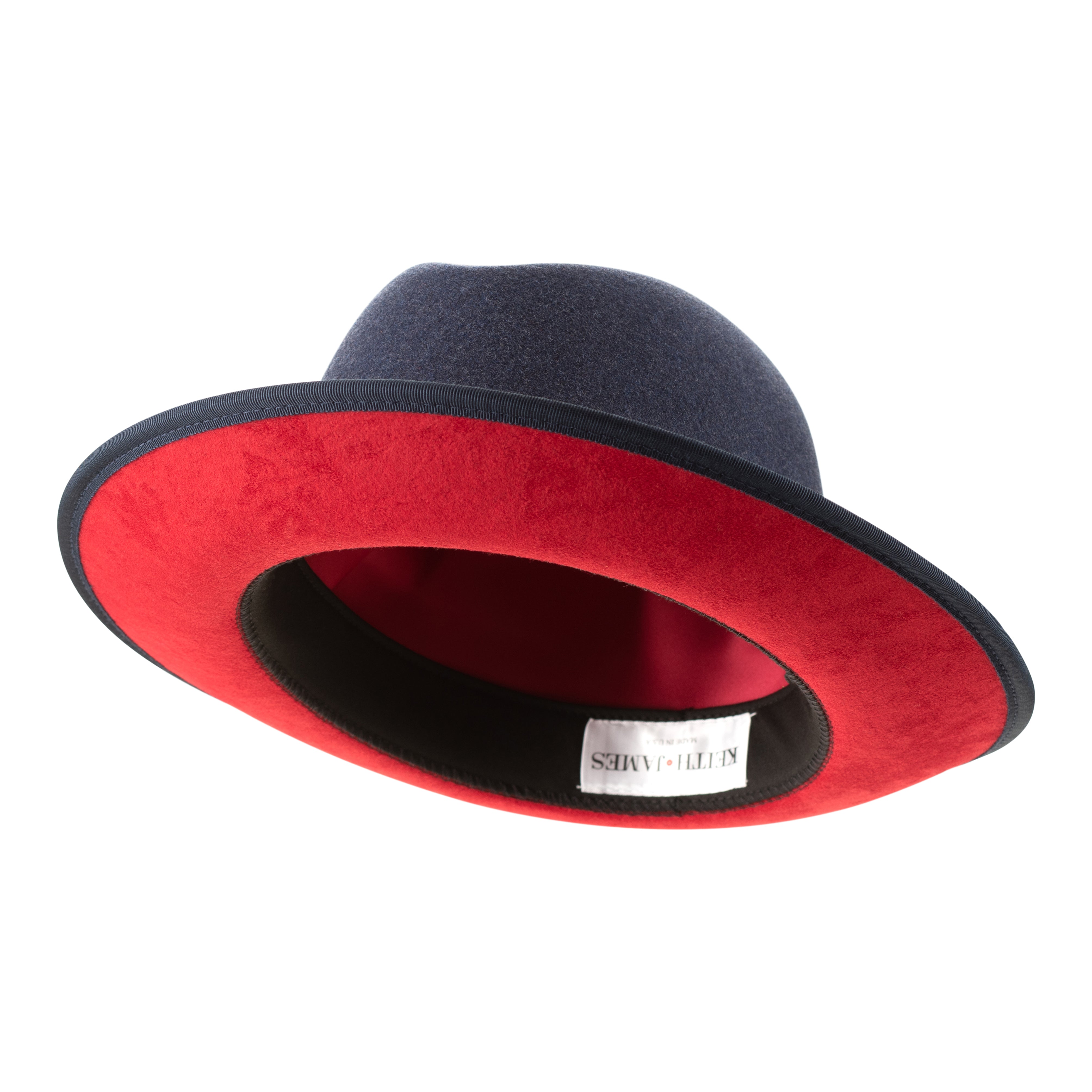 A denim blue classic center-creased fedora with a 2.5 inch curved brim and a red bottom trim, featuring a classic ribbon trim and a signature logo pin.