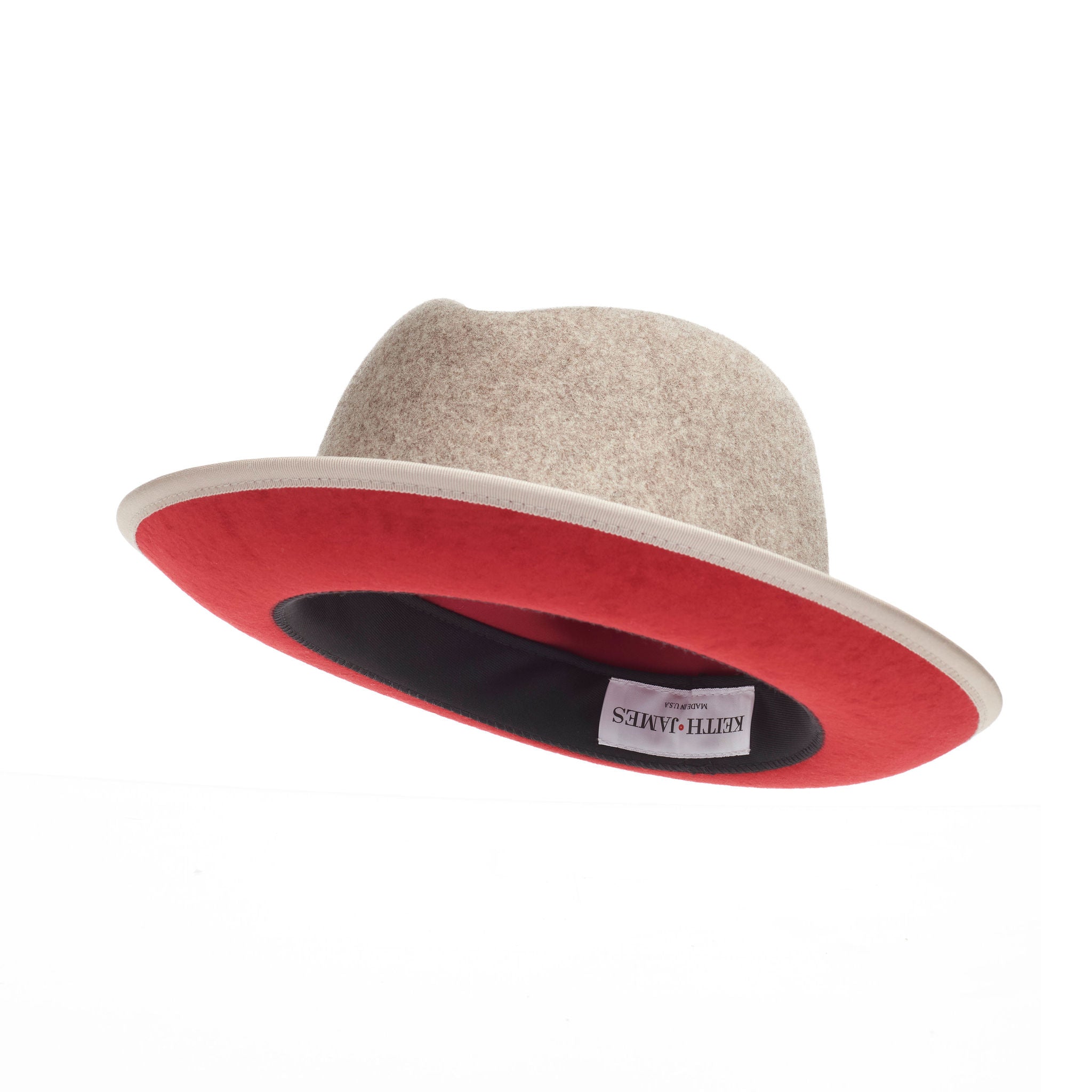 A beige fedora hat with a red bottom brim and a signature logo pin.