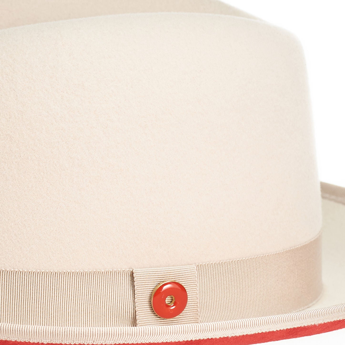 A sandy beige fedora with a red bottom brim and a signature logo pin.