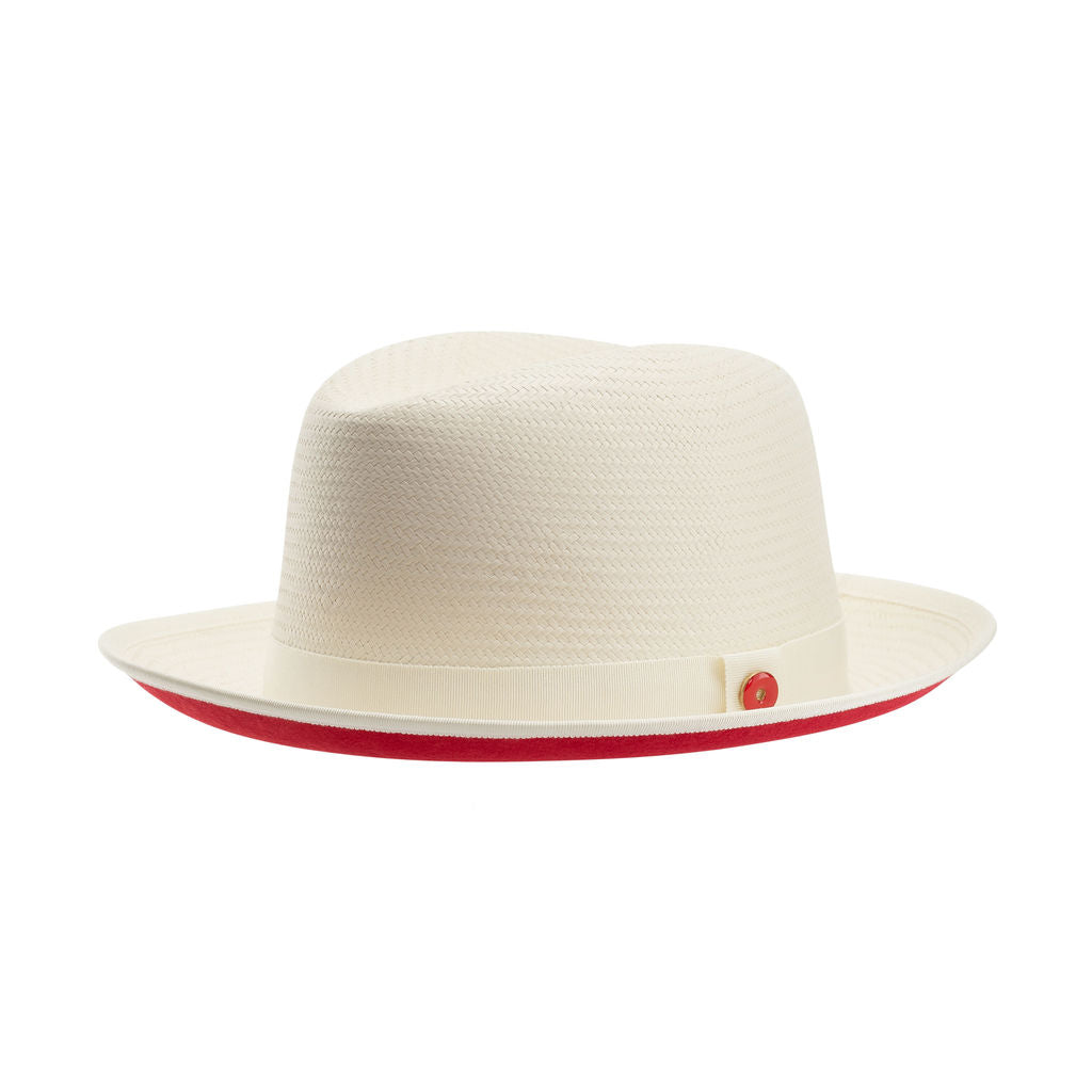 A beige classic fedora hat with a red bottom brim and a signature logo pin.