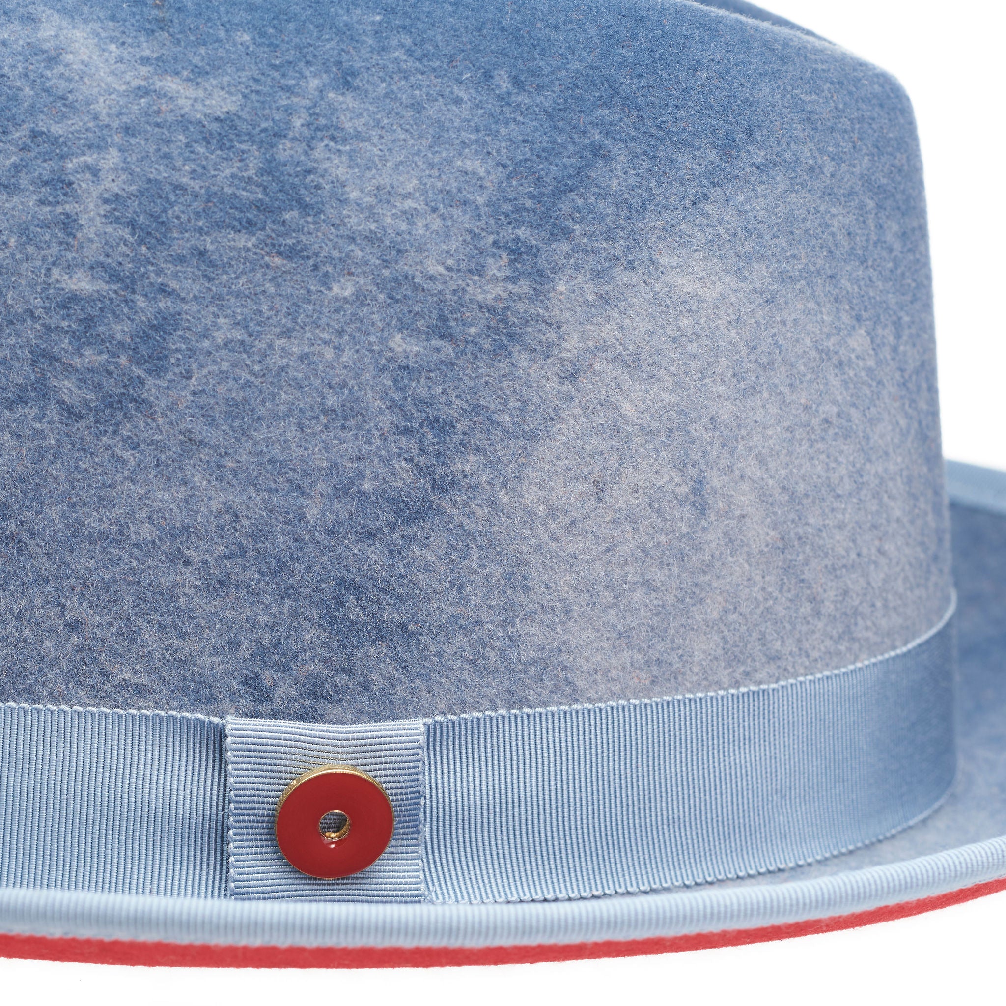 A blue fedora with a red bottom brim and a signature logo pin.