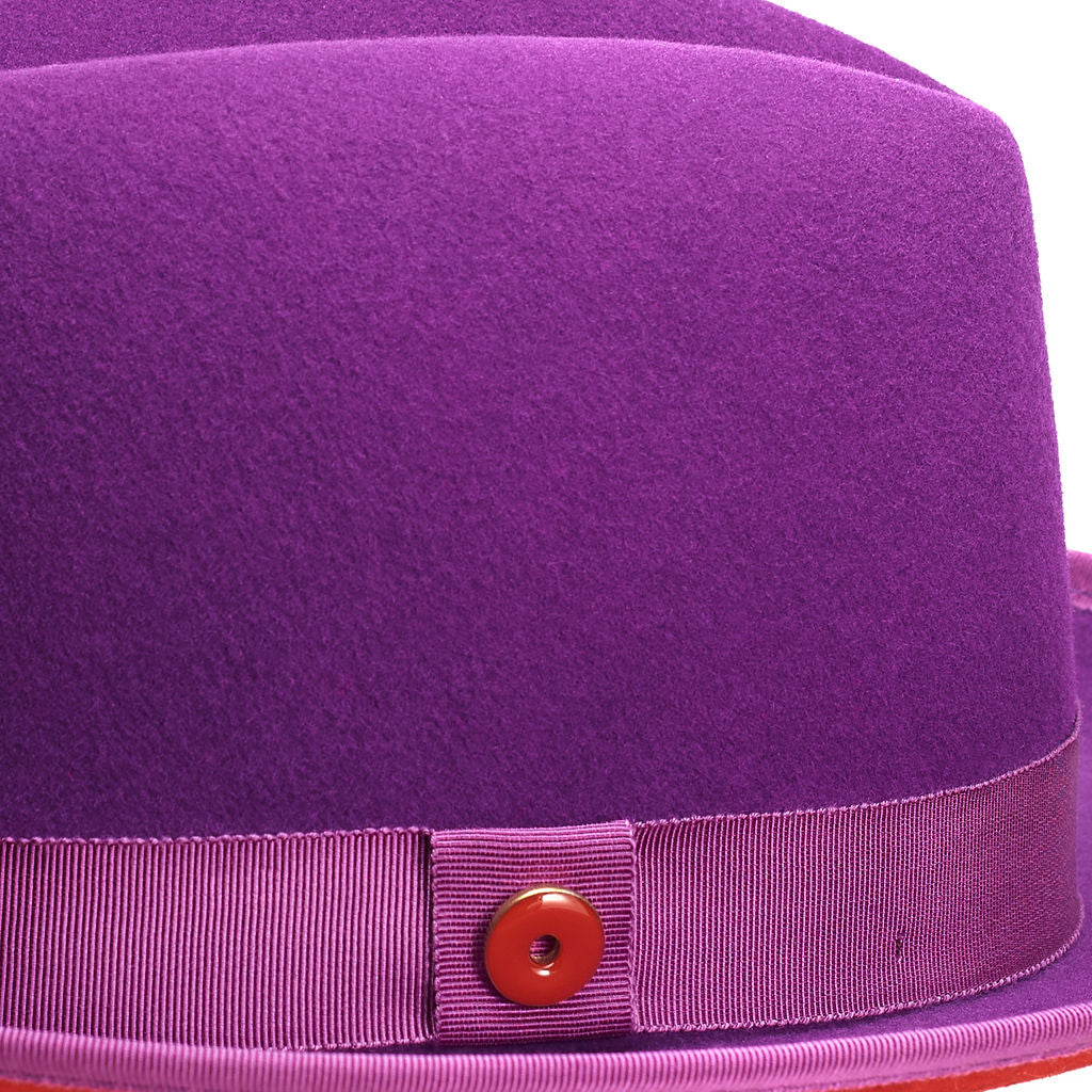 A violet purple classic center-creased fedora with a 2.5 inch curved brim, signature logo pin, and red bottom brim.