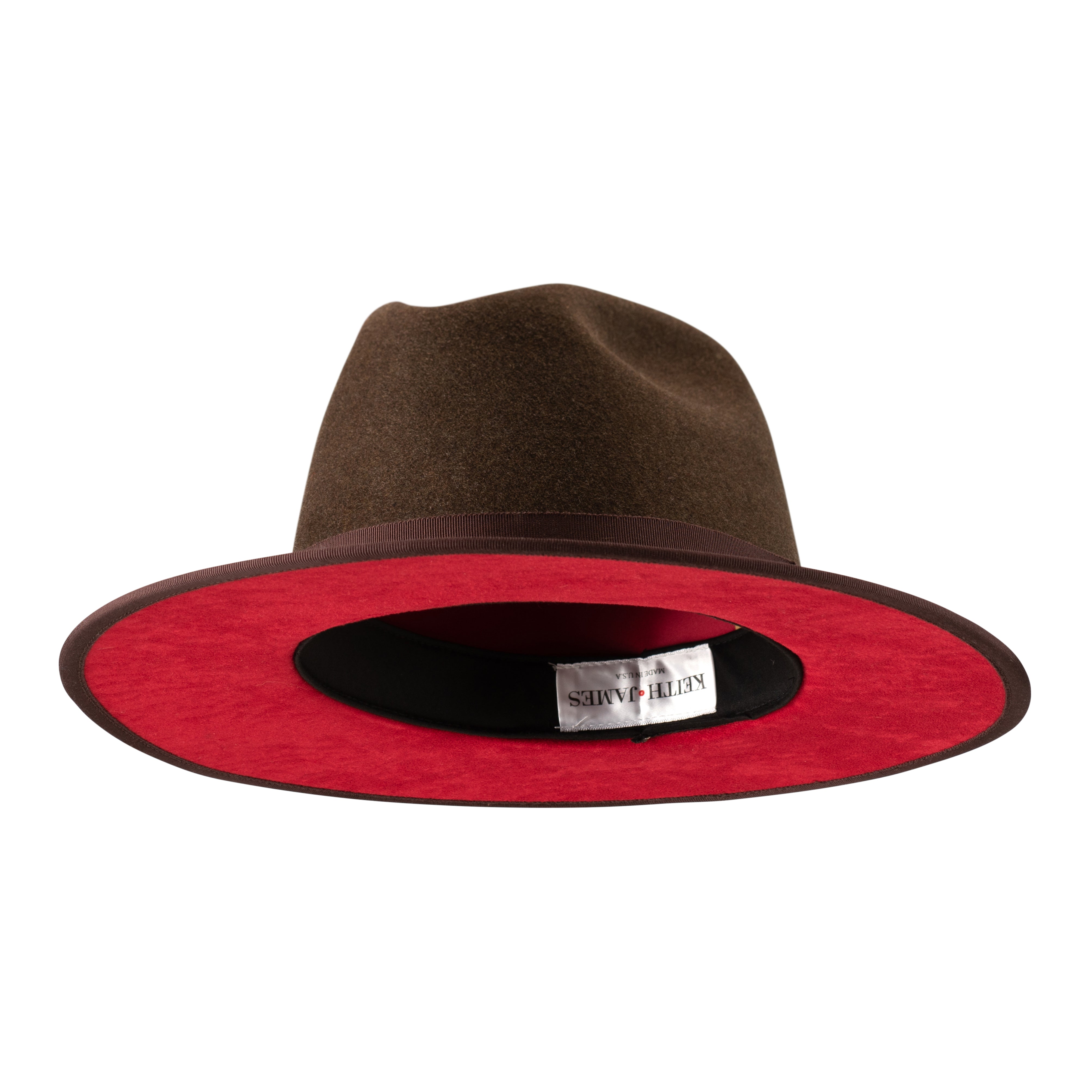 A cocoa brown fedora hat with a flat brim and a classic ribbon trim, featuring a signature logo pin on the crown and a red bottom brim.
