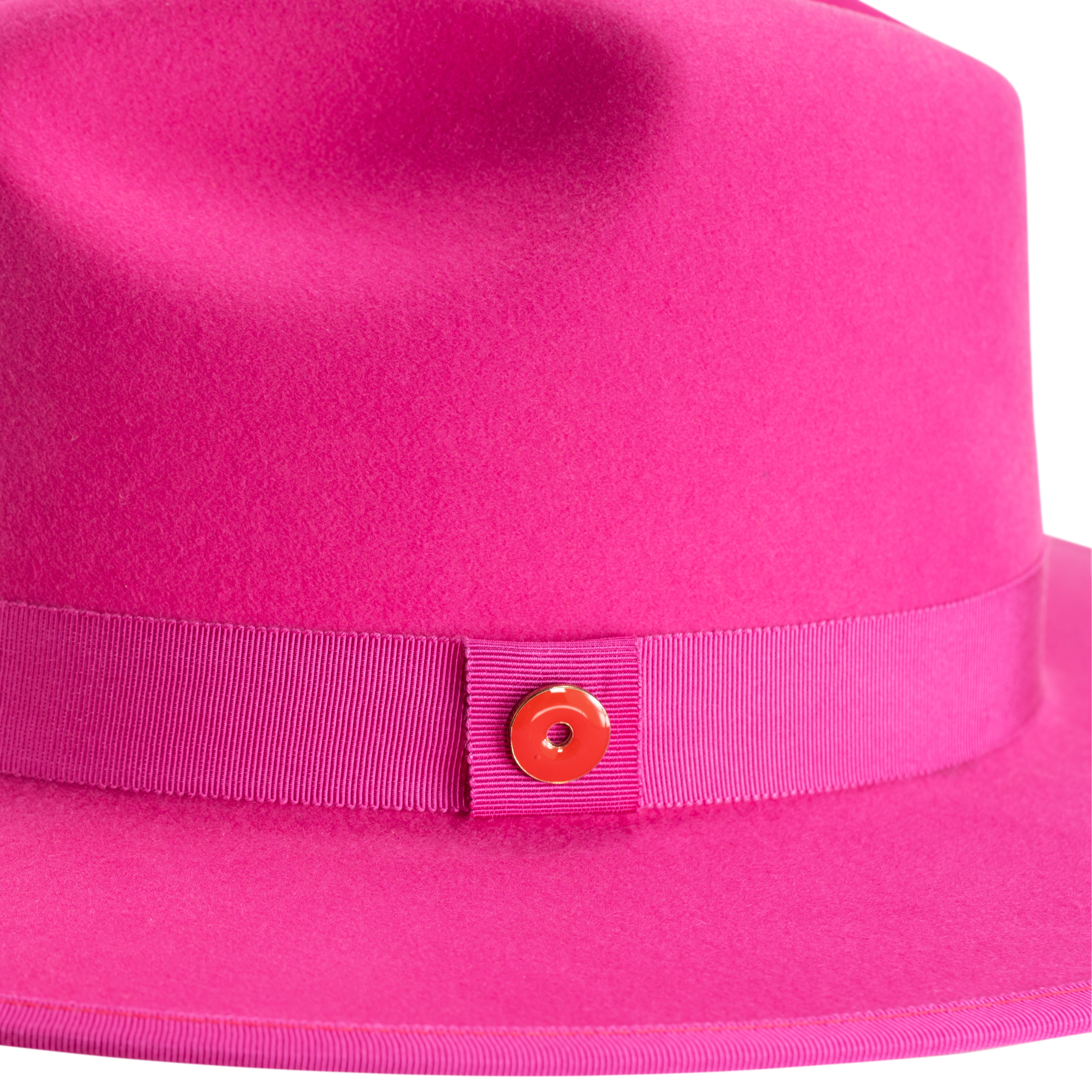 A hot pink fedora hat with a flat brim, classic ribbon trim, and a signature logo pin on the side.