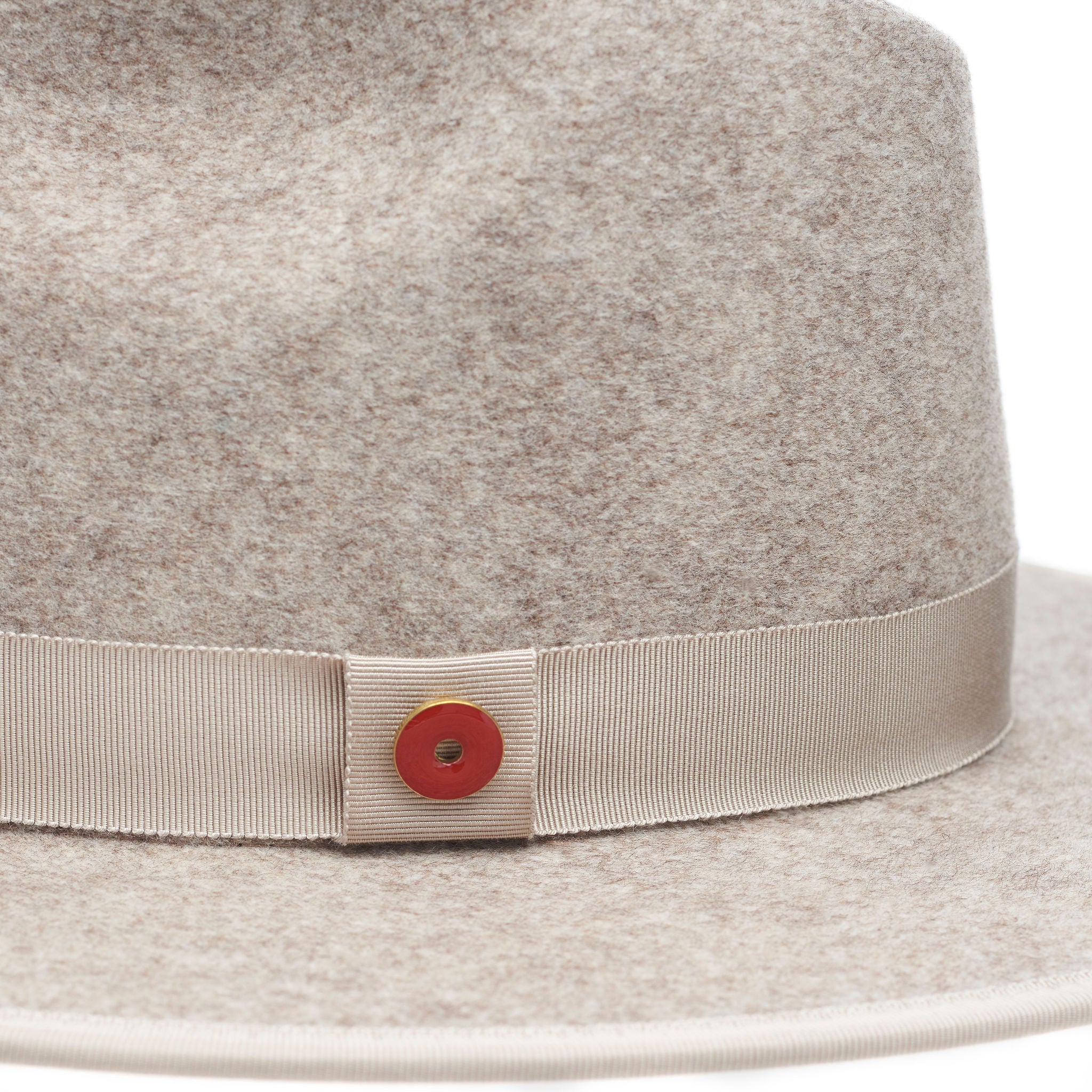 A beige pinched crown fedora hat with a flat brim and a classic ribbon trim, featuring a signature logo pin and a red bottom brim.