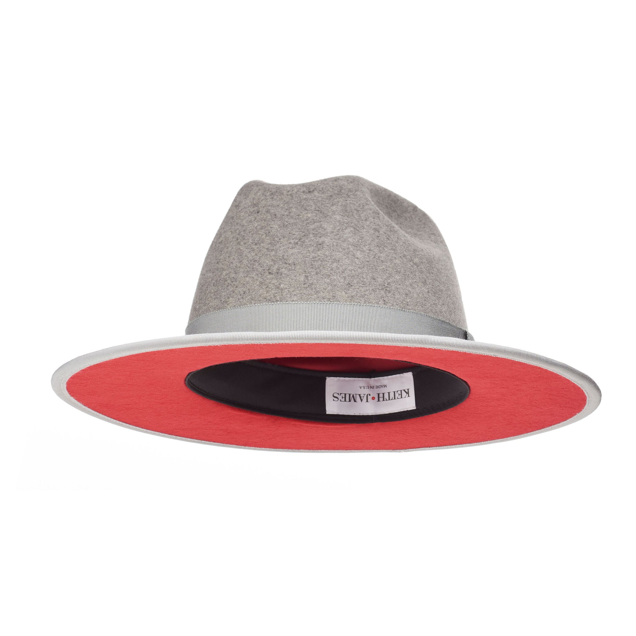 A grey fedora hat with a flat brim and a classic ribbon trim, featuring a signature logo pin and a red bottom brim.