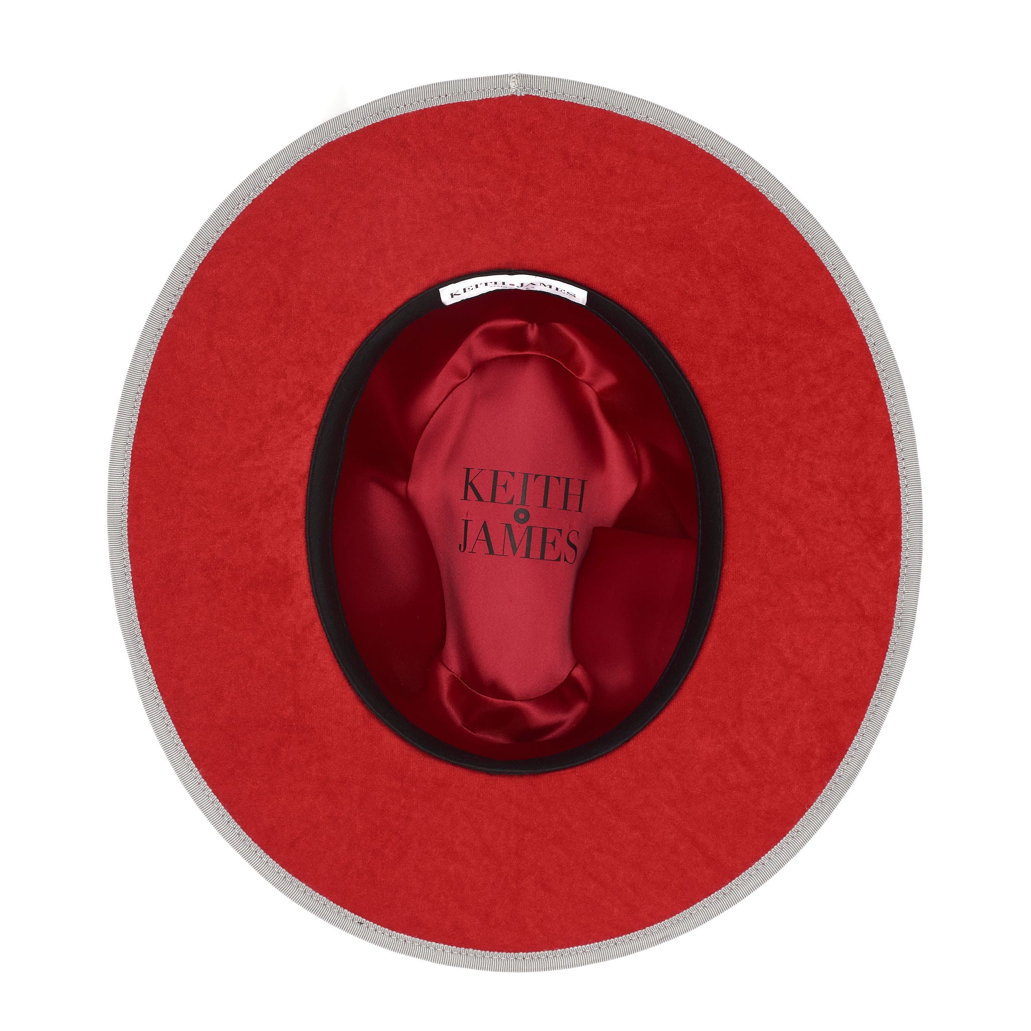 A grey pinched crown fedora hat with a flat brim and a classic ribbon trim, featuring a signature logo pin and a red bottom brim.