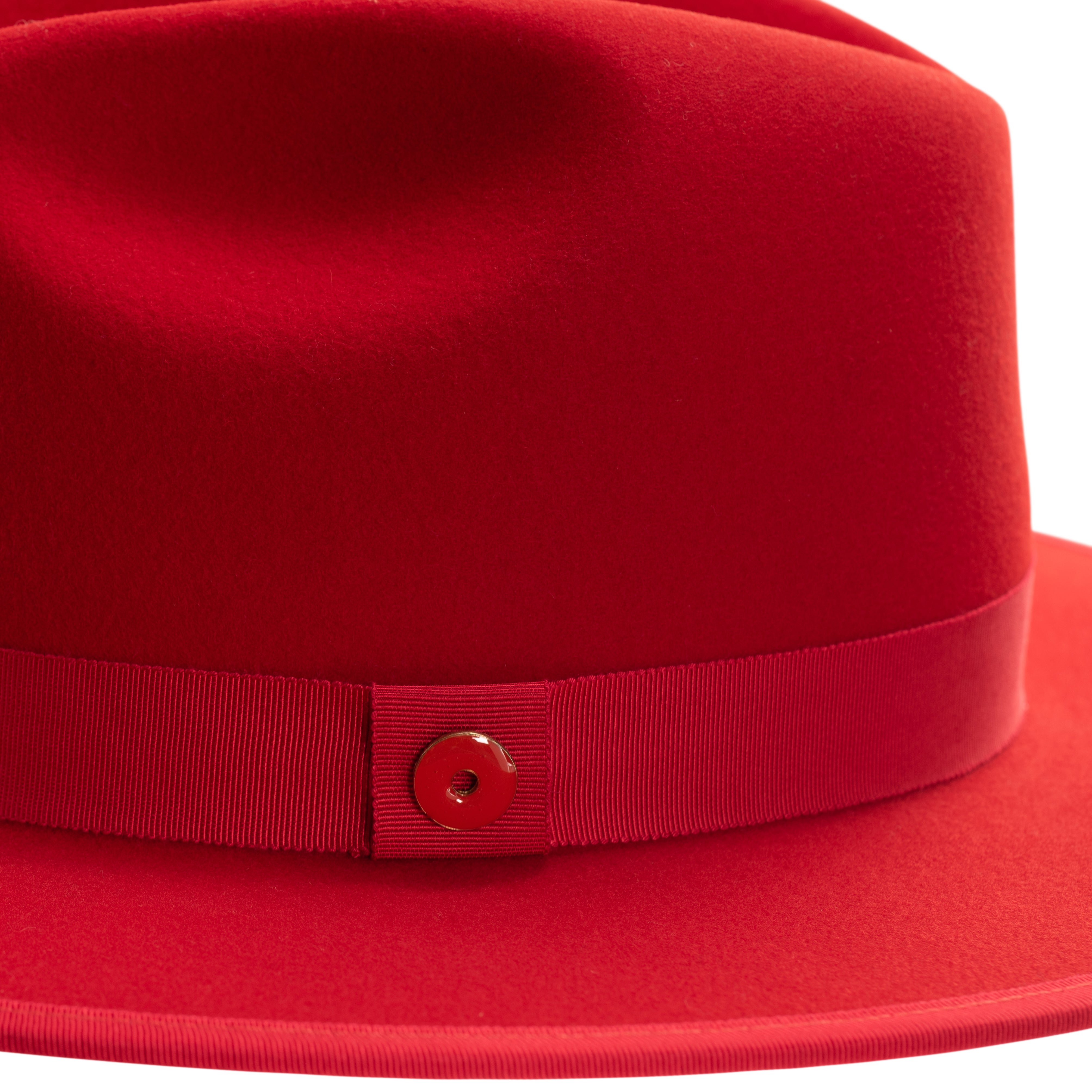 A rose red fedora hat with a pinched crown, flat brim, and bound edge. It includes a classic ribbon trim, a signature logo pin, and a red bottom brim.