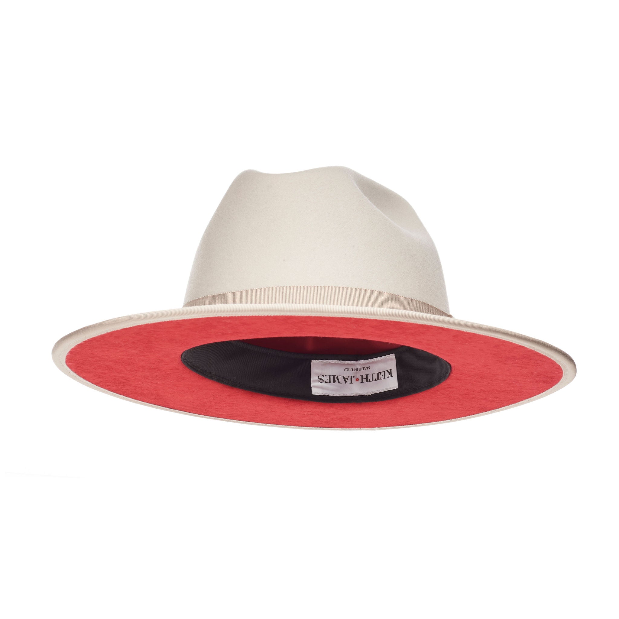 A sandy beige fedora hat with a flat brim and classic ribbon trim, featuring a signature logo pin and red bottom brim.