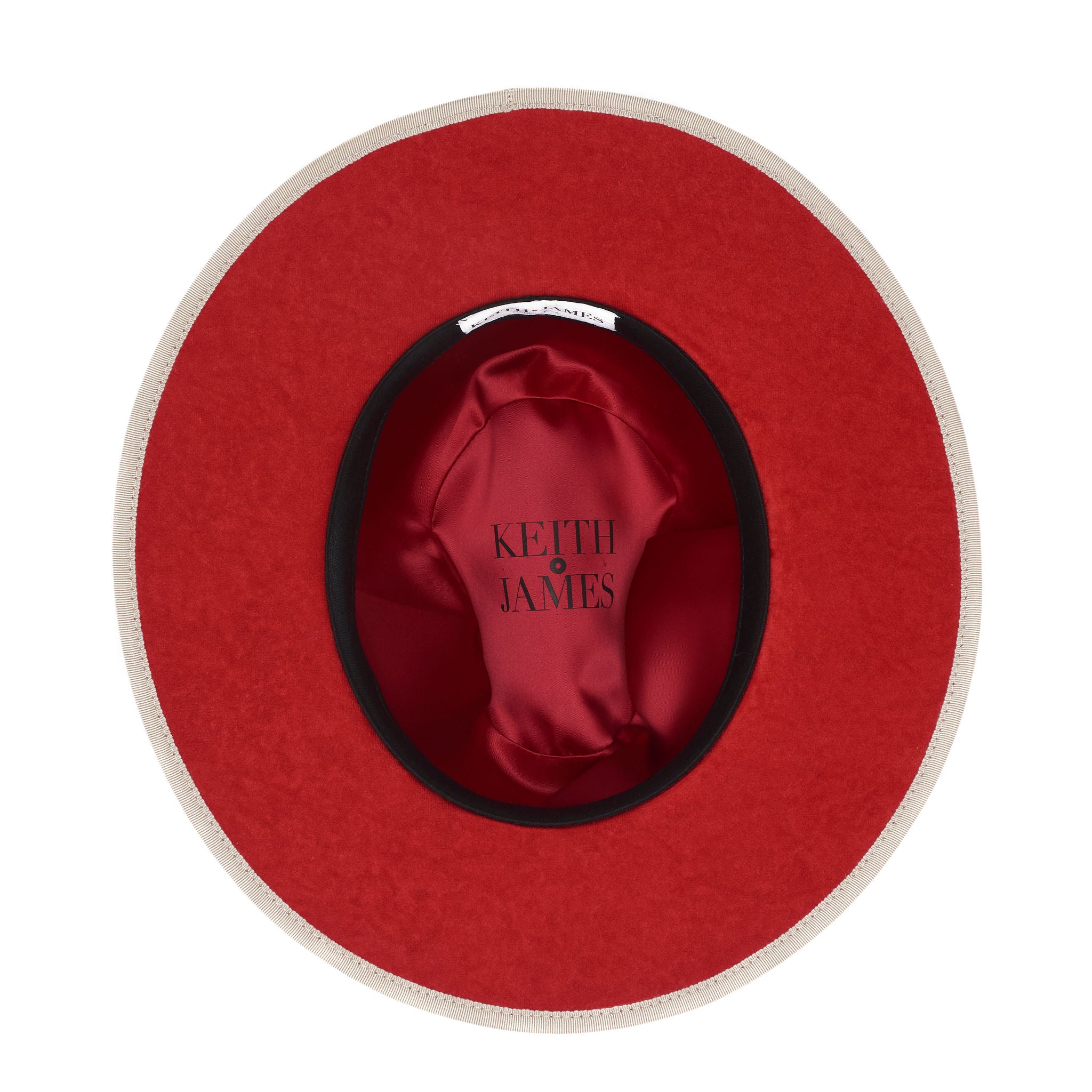 A beige pinched crown fedora hat with a flat brim and a classic ribbon trim, featuring a signature logo pin and a red bottom brim.