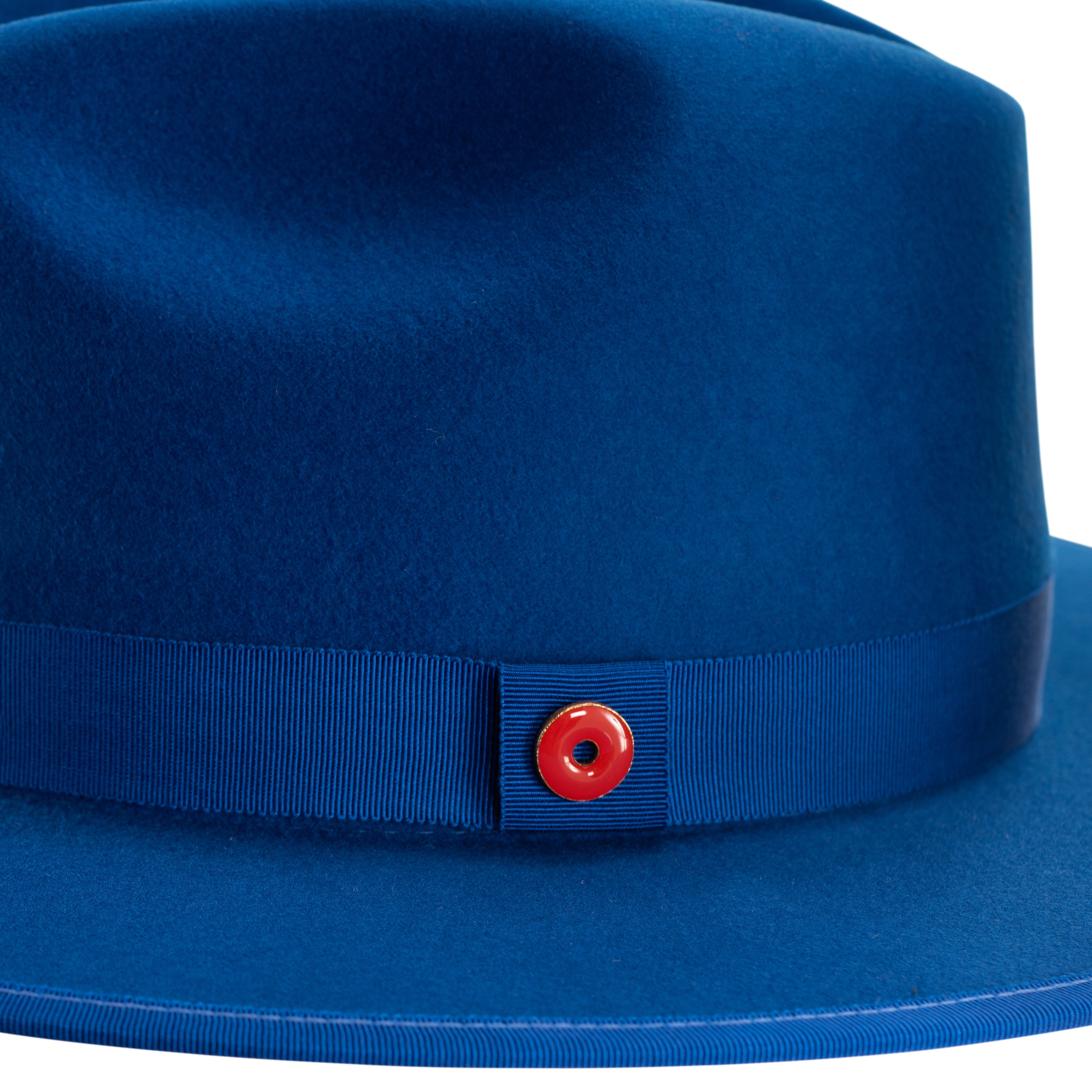 A true blue fedora hat with a pinched crown, flat brim, and bound edge. It includes a classic ribbon trim, a signature logo pin, and a red bottom brim.