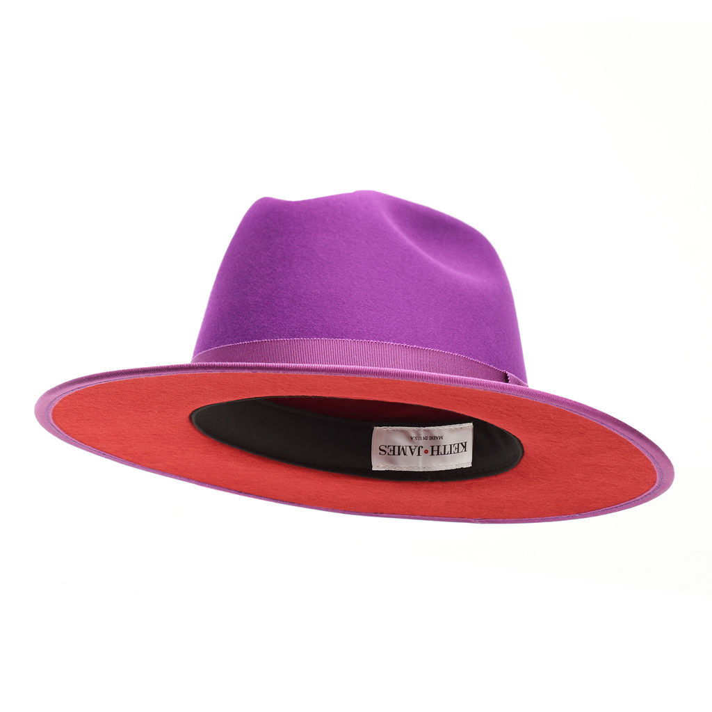 A violet purple fedora hat with a flat brim and a classic ribbon trim, featuring a signature logo pin and a red bottom brim.