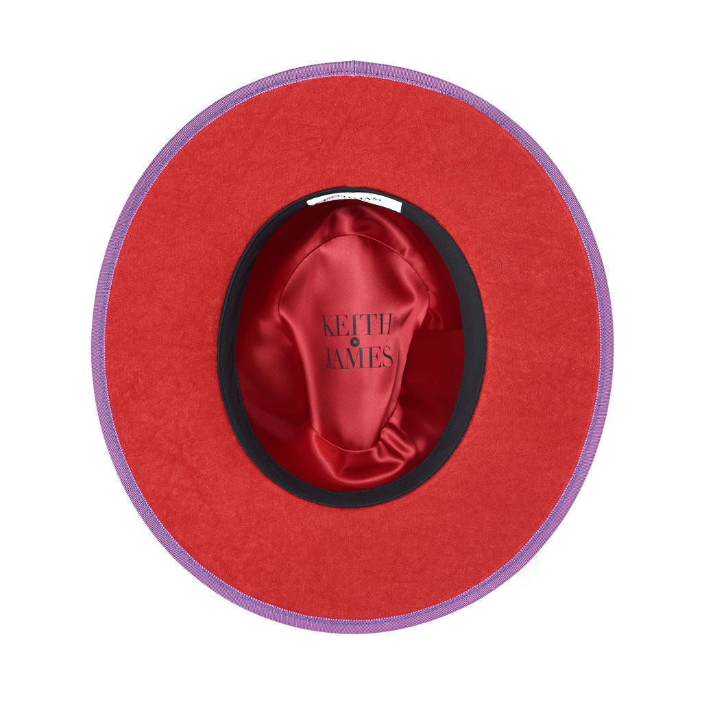 A violet purple fedora hat with a flat brim and a classic ribbon trim, featuring a signature logo pin and a red bottom brim.