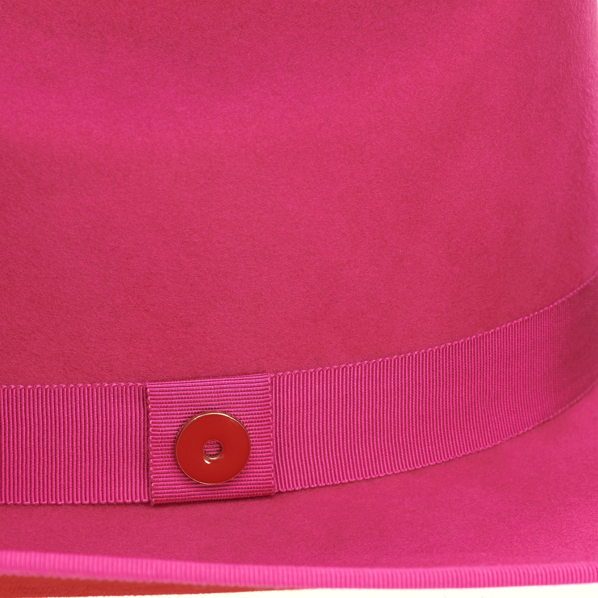 A hot pink cowboy hat with a red suede brim and a logo pin.