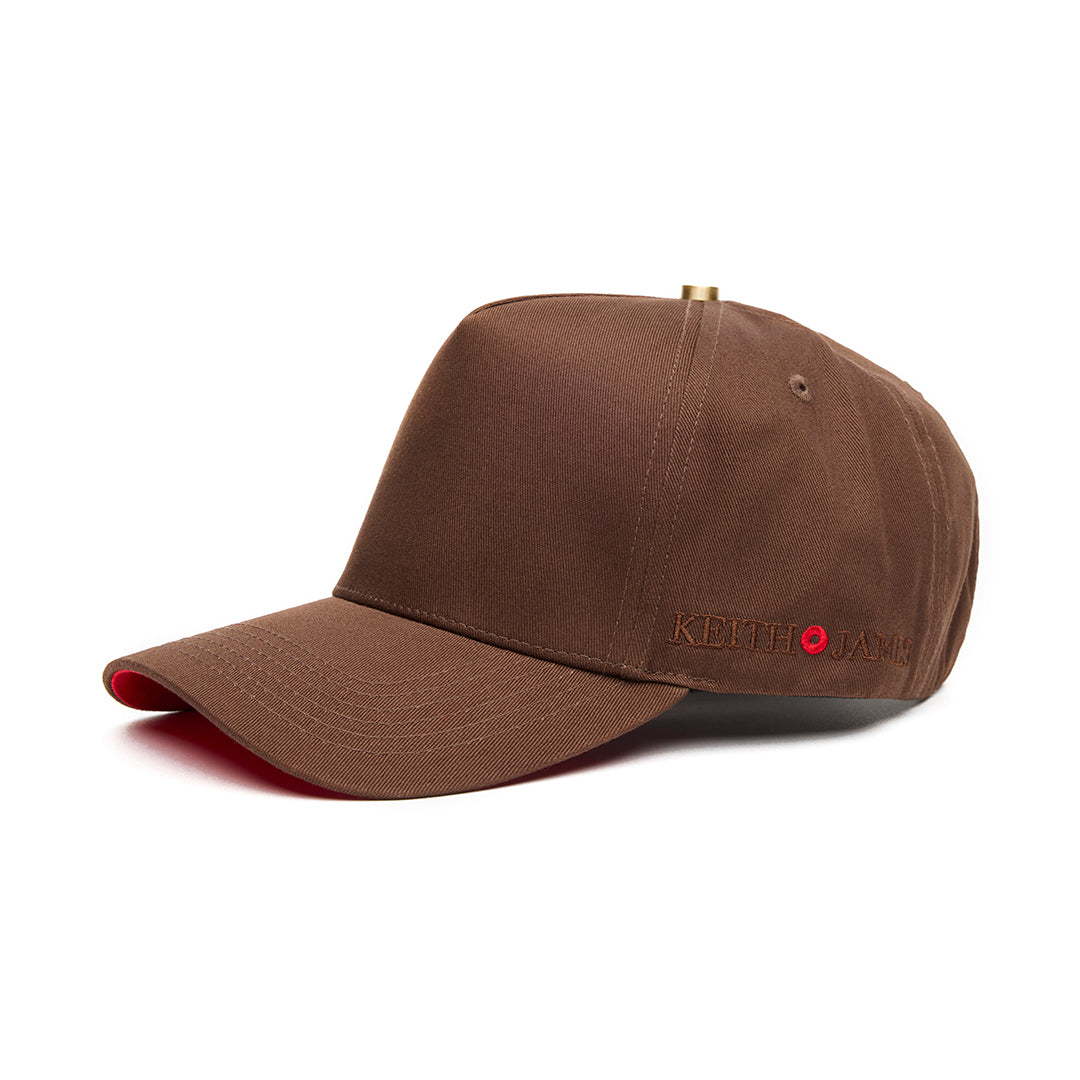 A cocoa brown 5 panel baseball cap with an adjustable band and a red bottom brim, featuring a logo embroidered on the front.