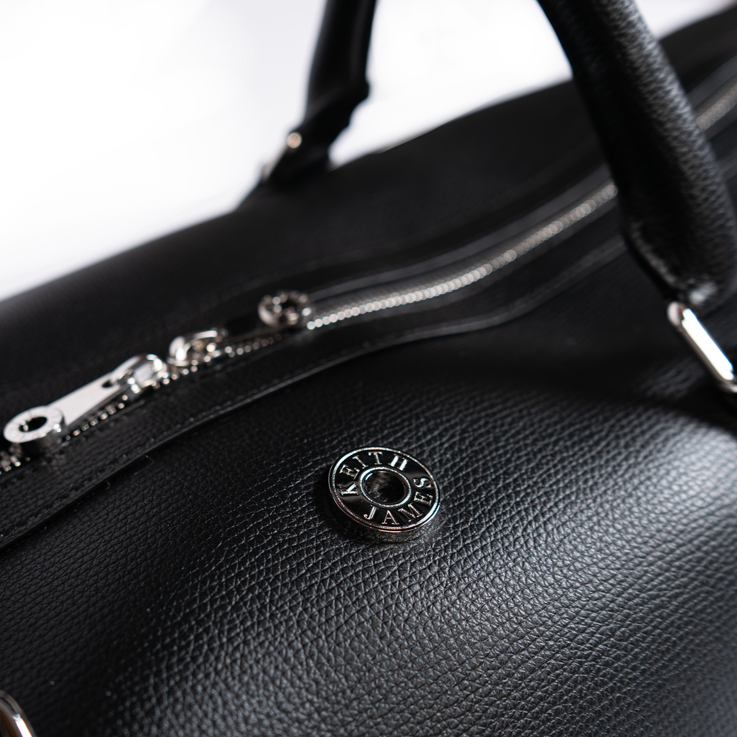 A jet black duffel bag with a detachable strap and gold-tone hardware on a white background.