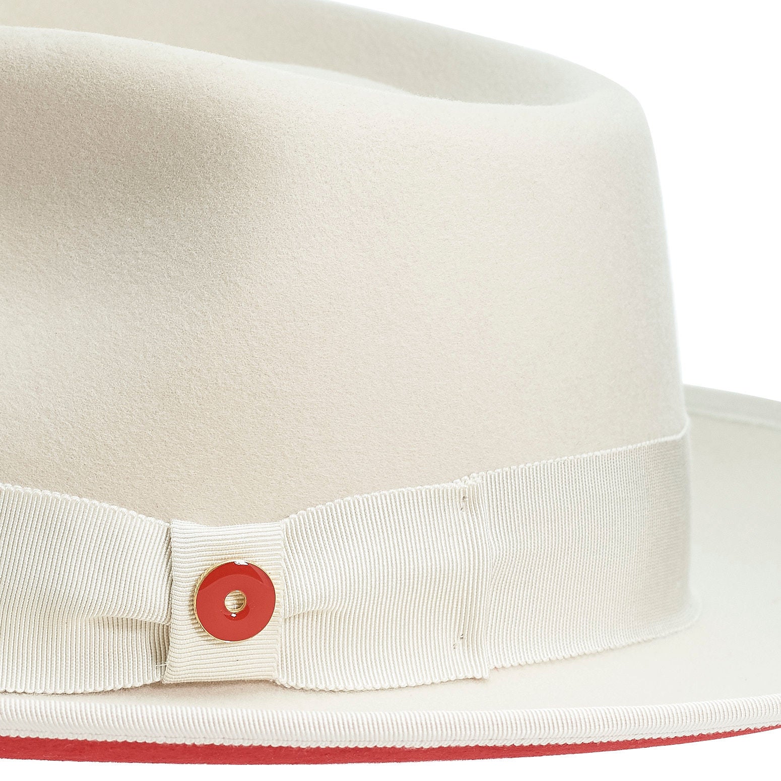 A sandy beige hat with a red bottom brim, a classic wide ribbon, and a bow signature logo pin.