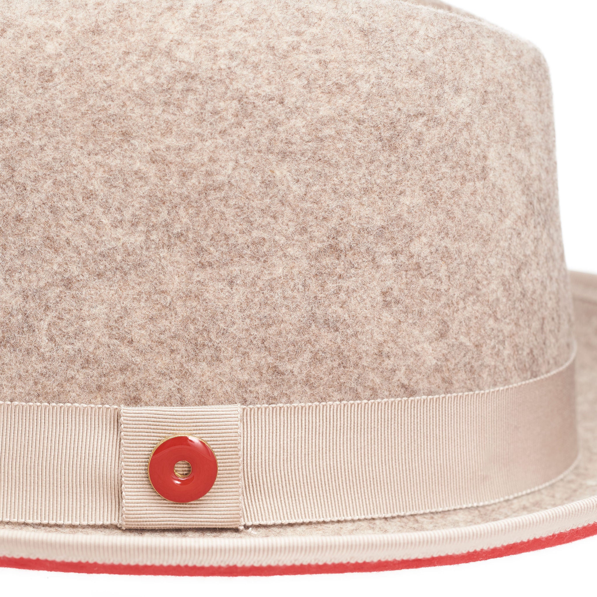A beige fedora hat with a red bottom brim and a signature logo pin.