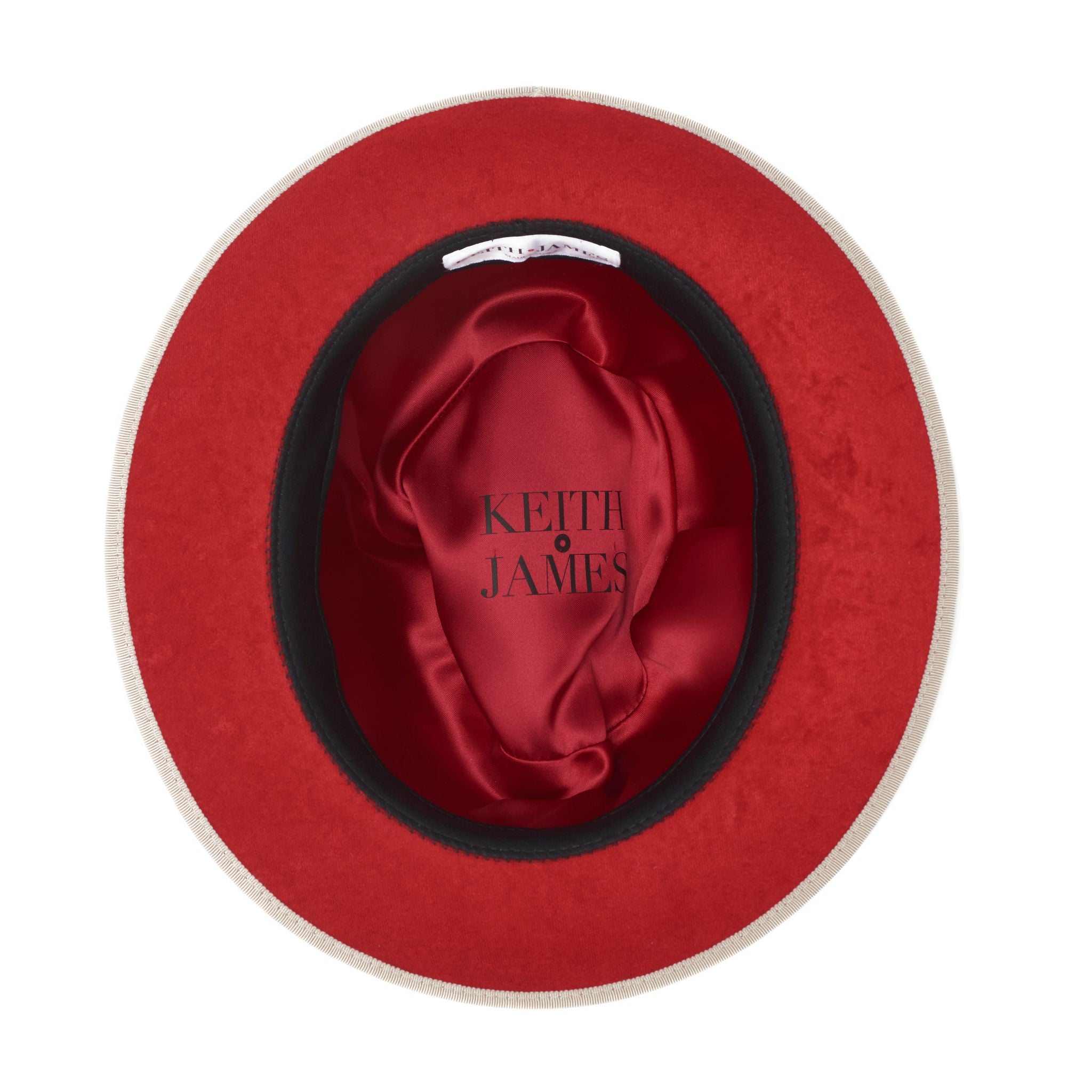 A beige fedora hat with a red bottom brim and a signature logo pin.