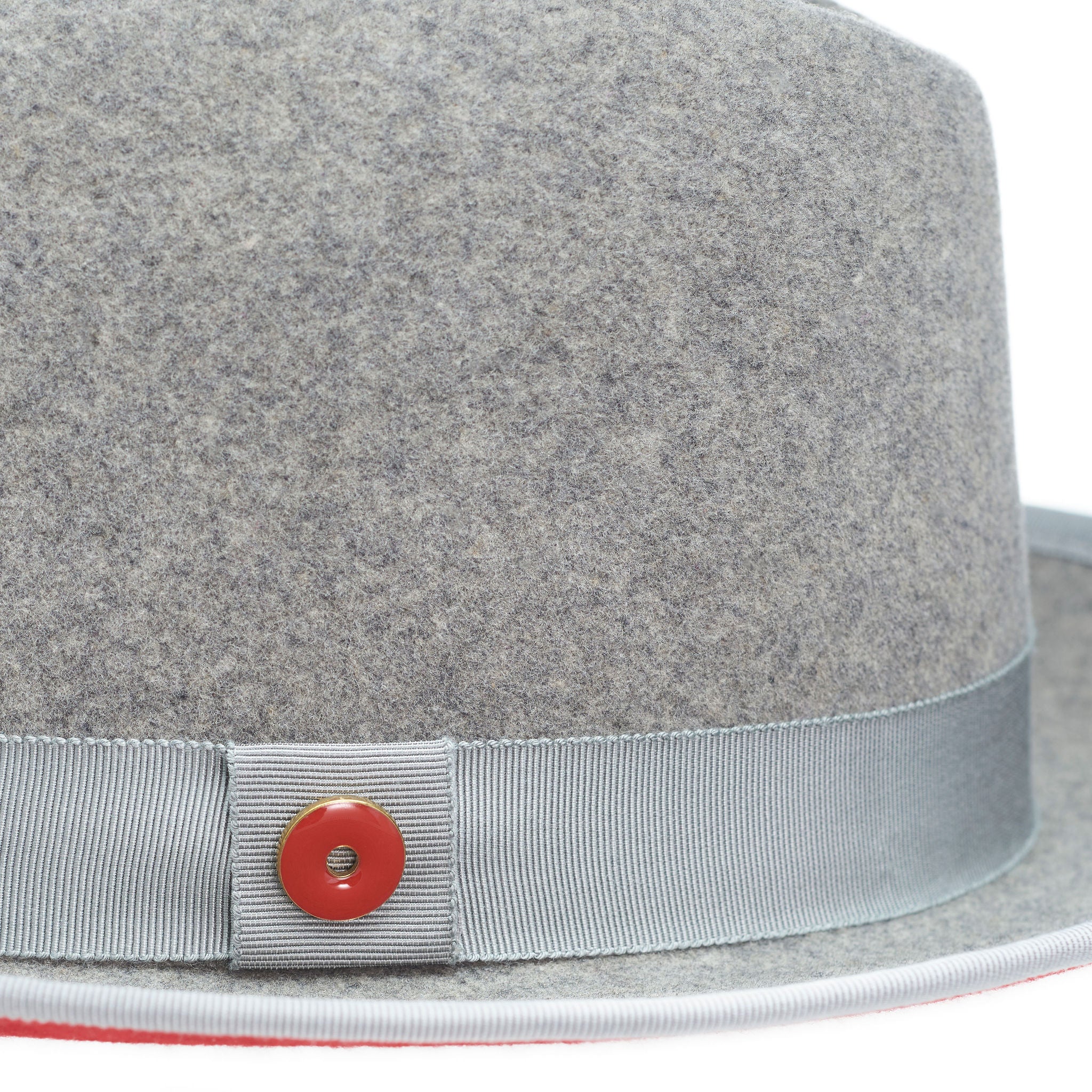 A gray fedora hat with a red bottom brim and a signature logo pin.