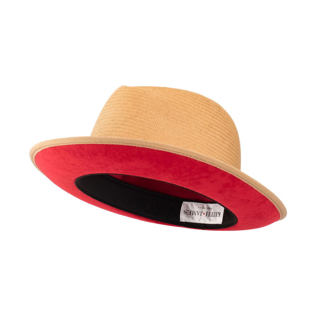 A golden honey straw fedora hat with a red bottom brim and a signature logo pin.
