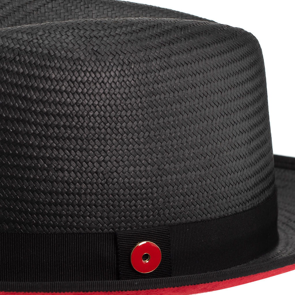A Jet Black straw fedora with a red under brim and a signature logo pin on the side.