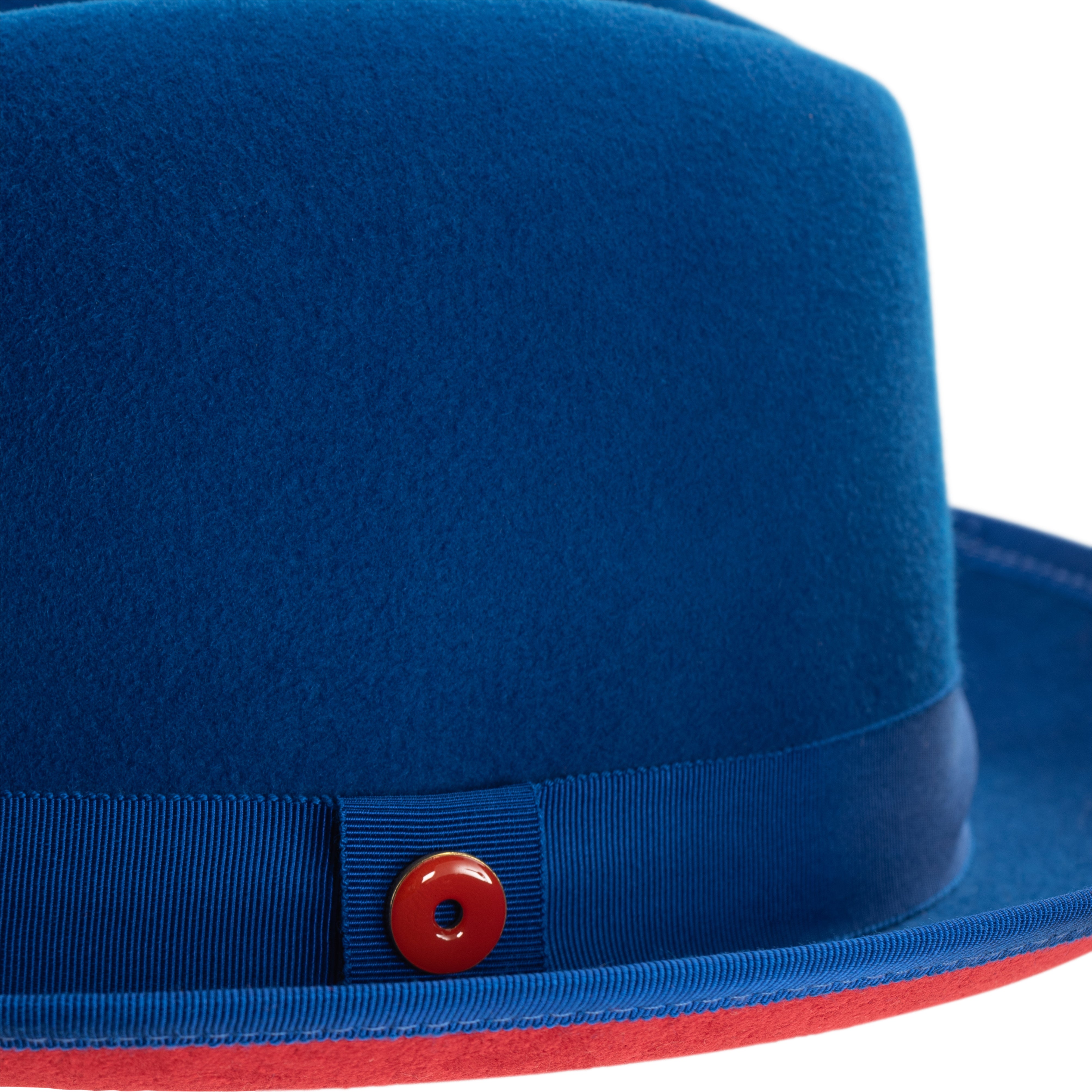 A blue fedora hat with a red bottom brim and a signature logo pin.