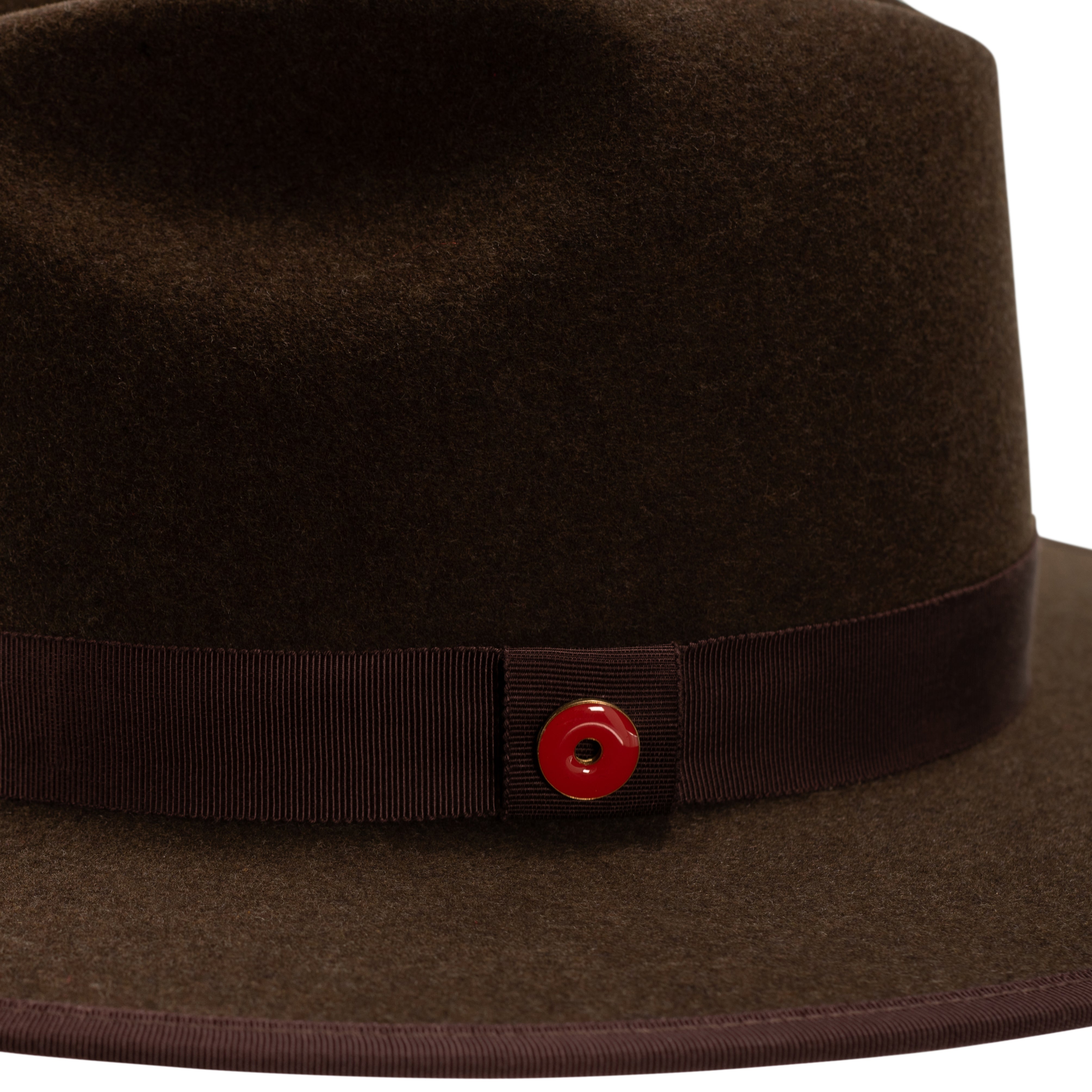 A cocoa brown fedora hat with a flat brim and a classic ribbon trim, featuring a signature logo pin on the crown and a red bottom brim.