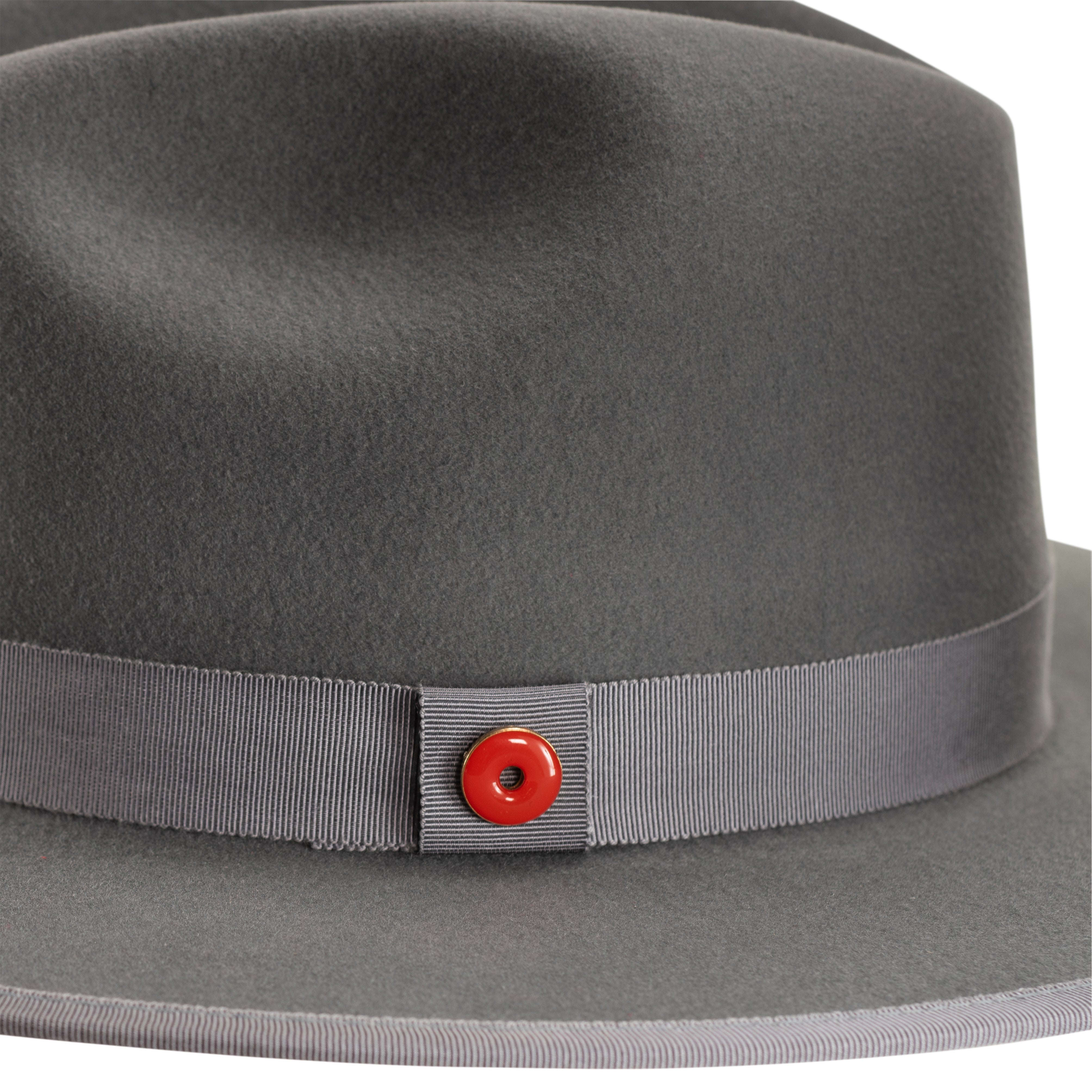 A cool grey pinched crown fedora hat with a flat brim and a classic ribbon trim, including a signature logo pin and red bottom brim.