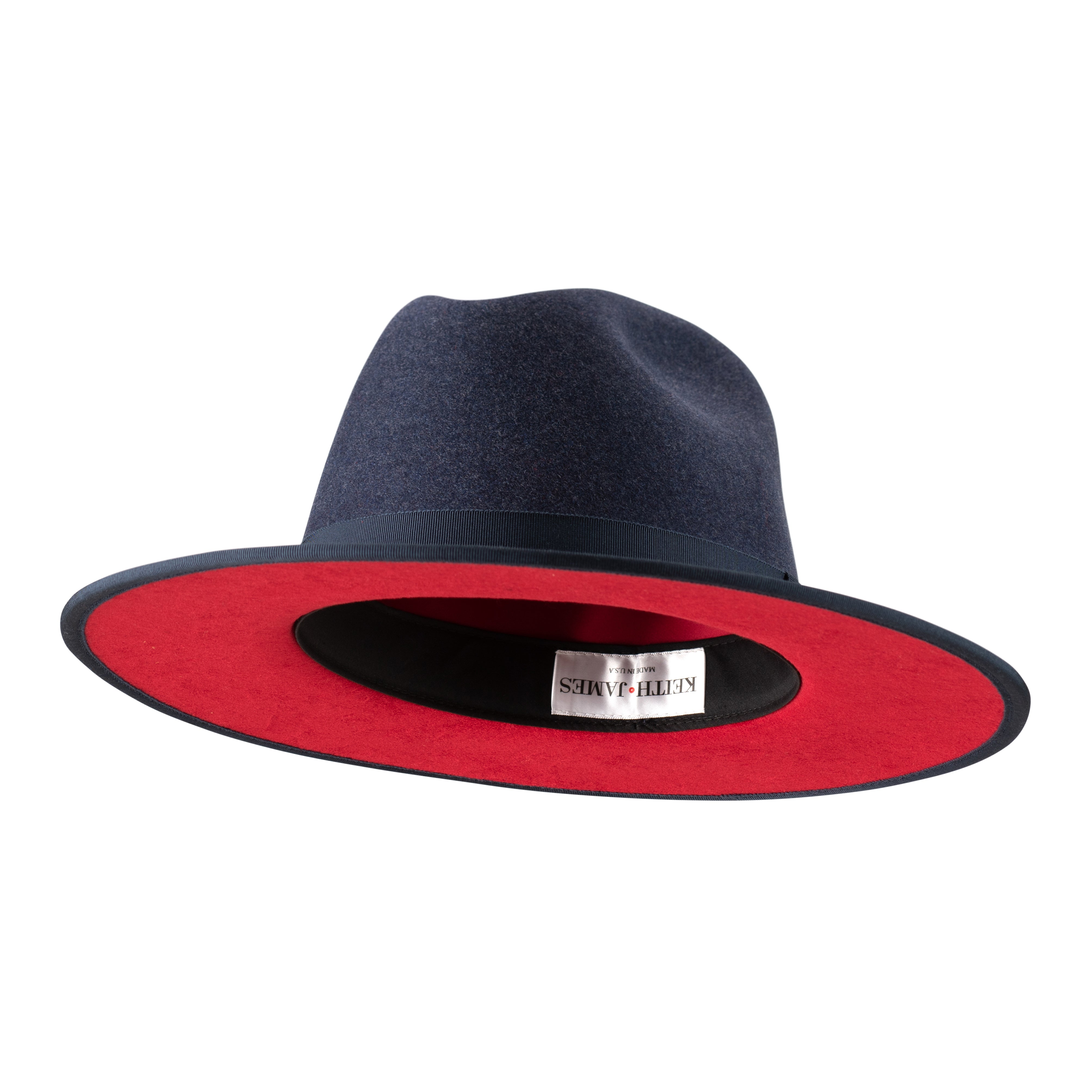A denim blue fedora hat with a pinched crown, flat brim, and bound edge. It includes a classic ribbon trim, a signature logo pin, and a red bottom brim.