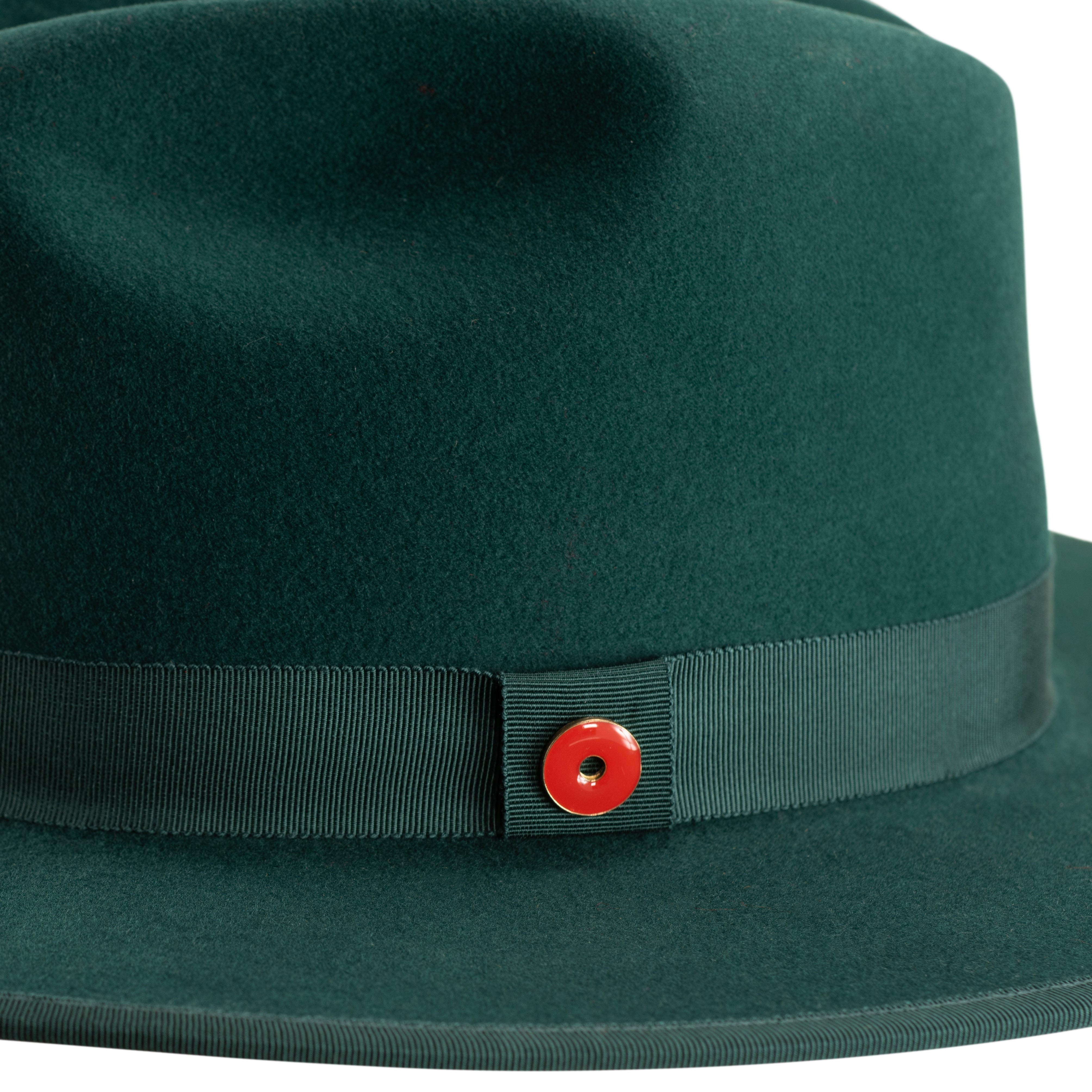 A green fedora hat with a flat brim and a classic ribbon trim, featuring a signature logo pin and a red bottom brim.