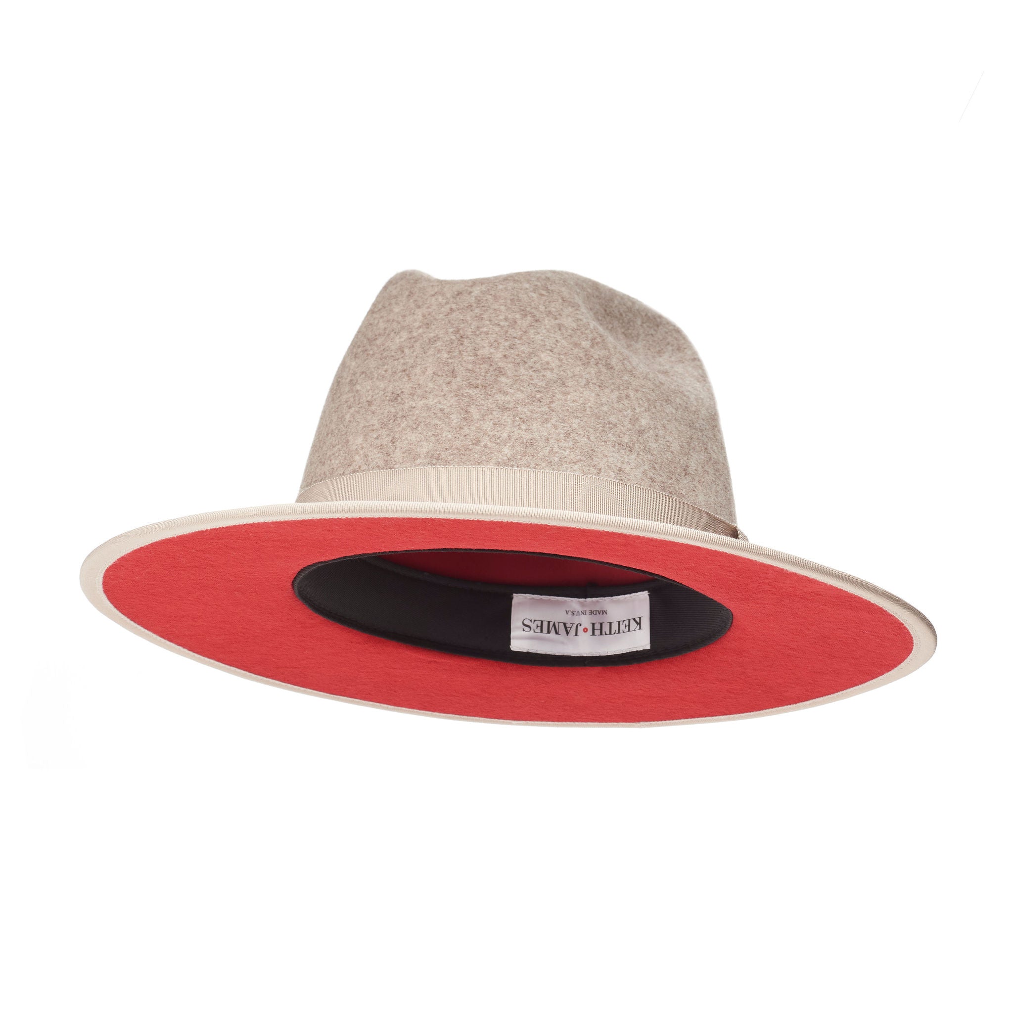 A beige pinched crown fedora hat with a flat brim and a classic ribbon trim, featuring a signature logo pin and a red bottom brim.