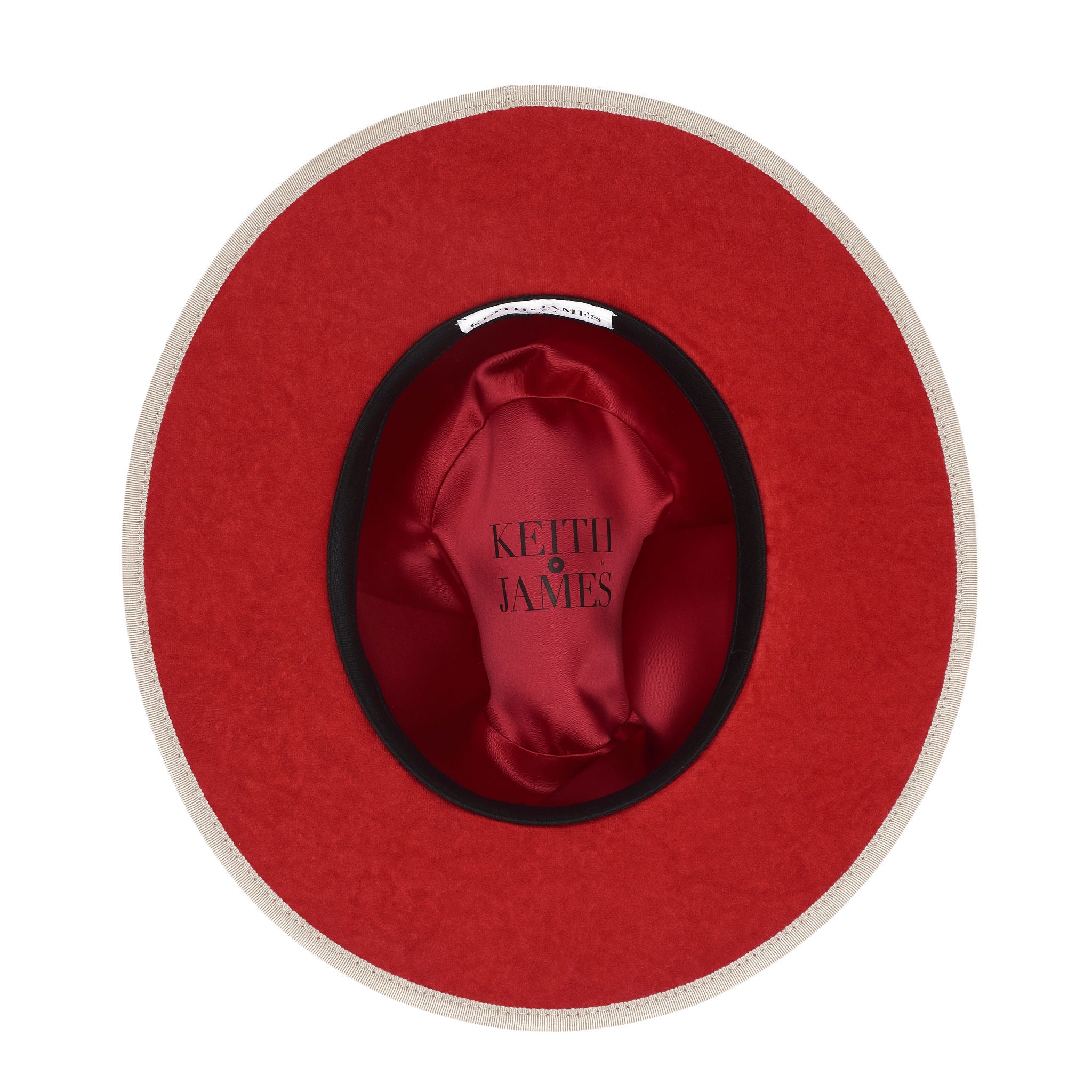 A beige pinched crown fedora hat with a flat brim and a classic ribbon trim, featuring a signature logo pin and a red bottom brim.