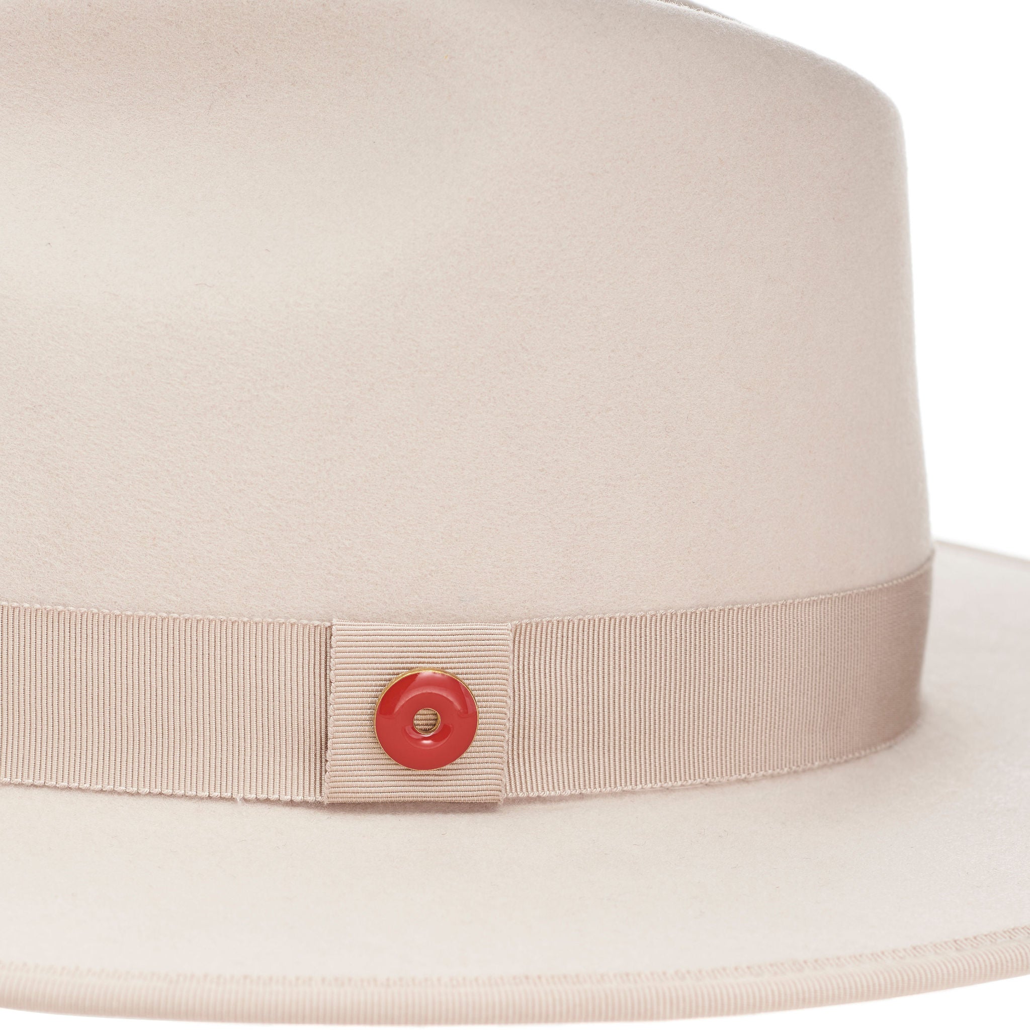 A sandy beige fedora hat with a flat brim and classic ribbon trim, featuring a signature logo pin and red bottom brim.