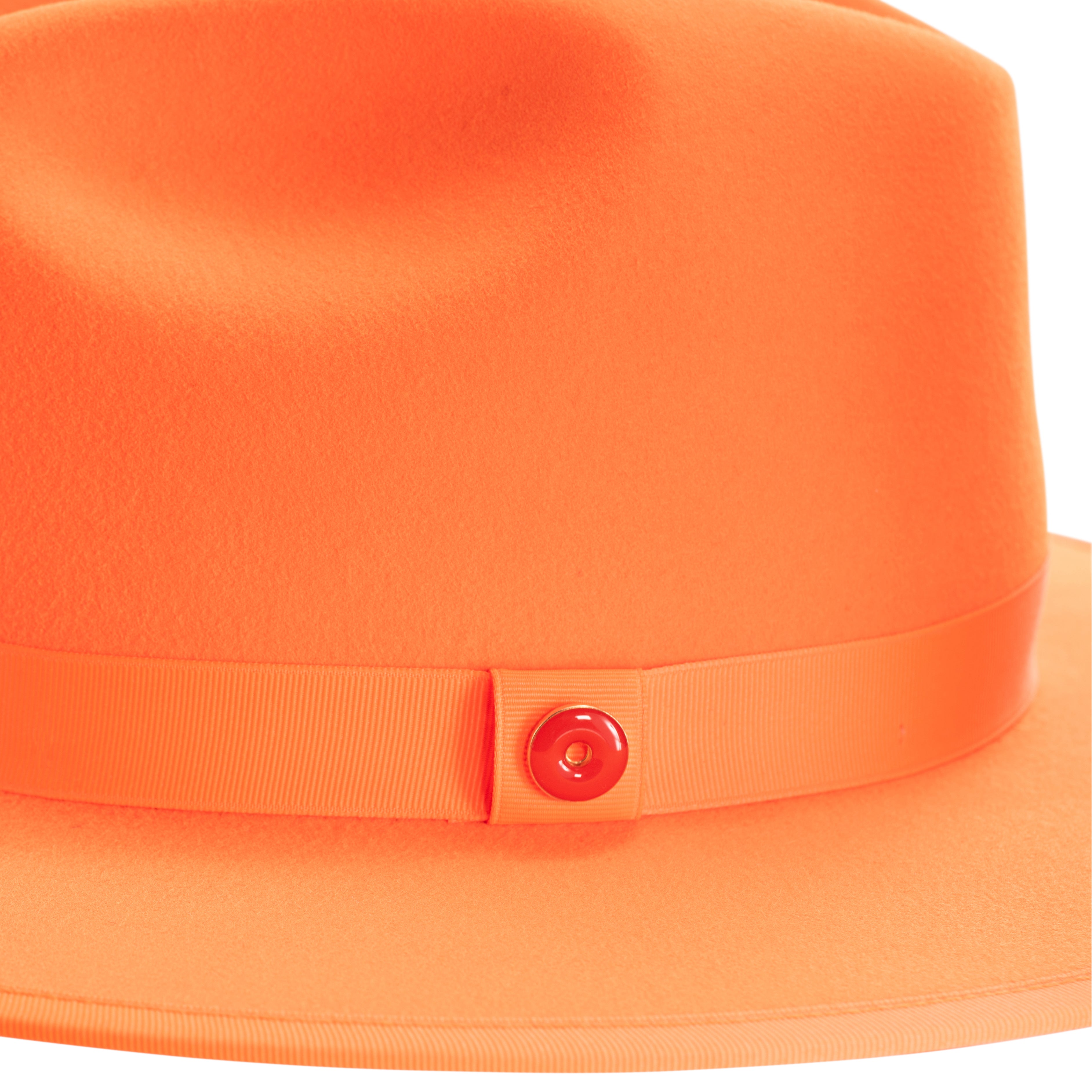 An orange fedora hat with a pinched crown and flat brim, featuring a classic ribbon trim and a signature logo pin on the front.