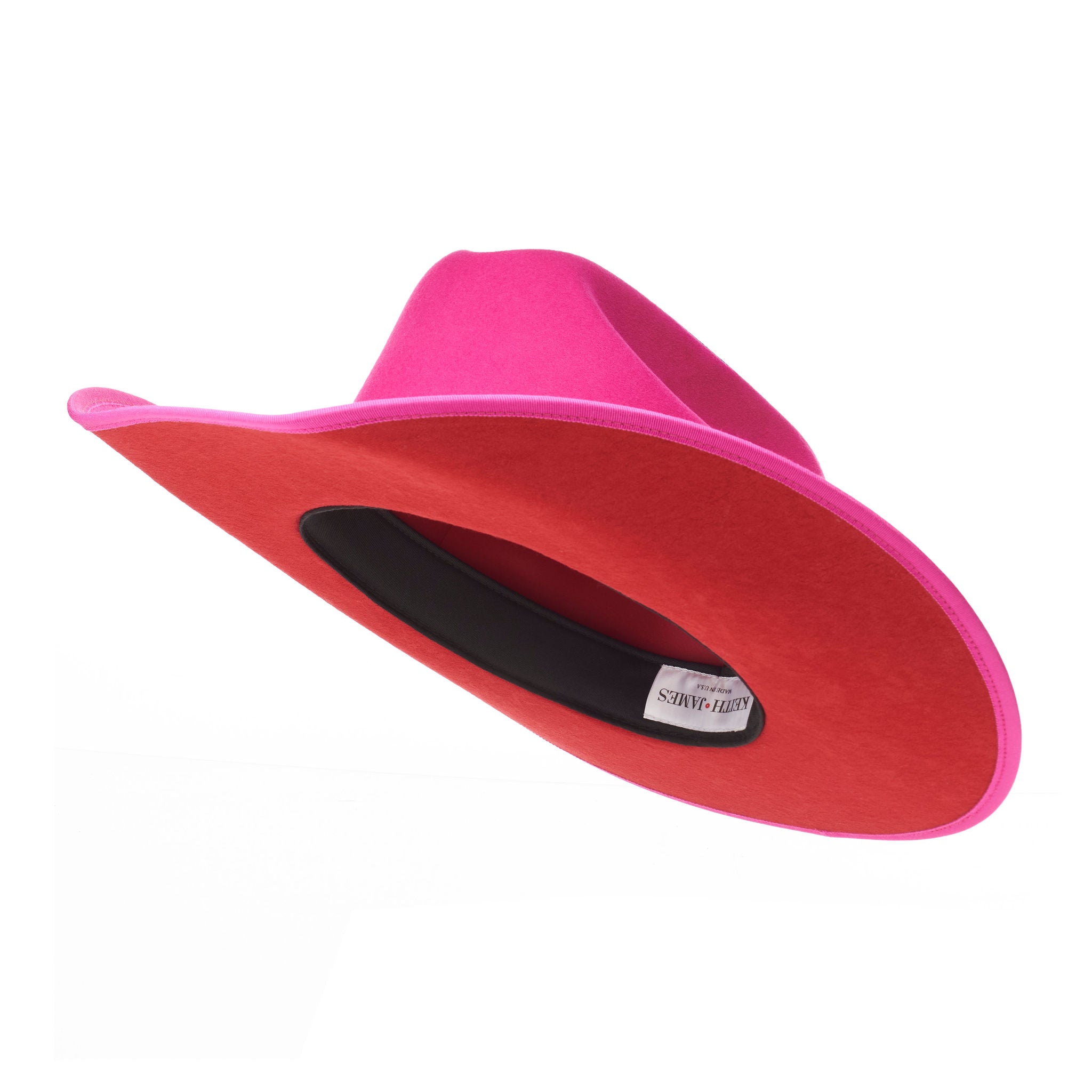 A hot pink cowboy hat with a red suede brim and a logo pin.